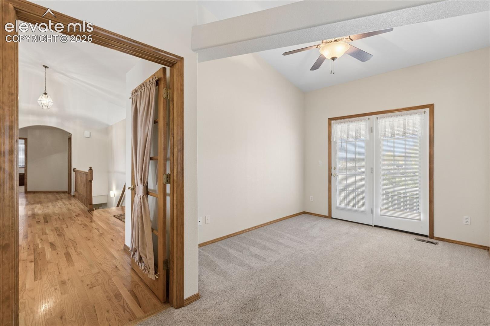 Vaulted ceilings, exposed structural beam, wood-finish flooring, glass-paned French doors, and ceiling fan with integrated lighting