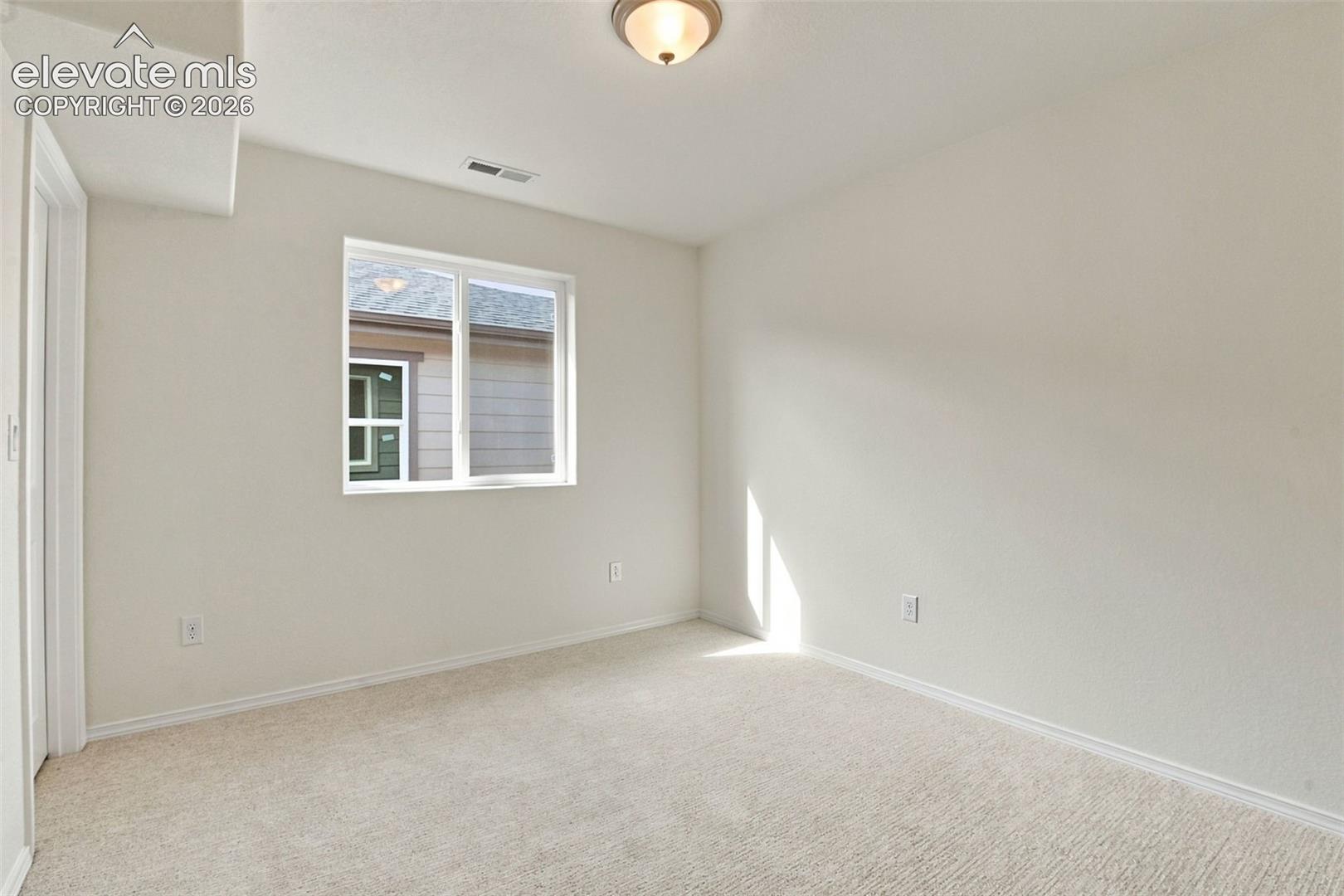 Neutral-toned interior space featuring wall-to-wall carpeting, a multi-pane window, and a flush-mount ceiling fixture
