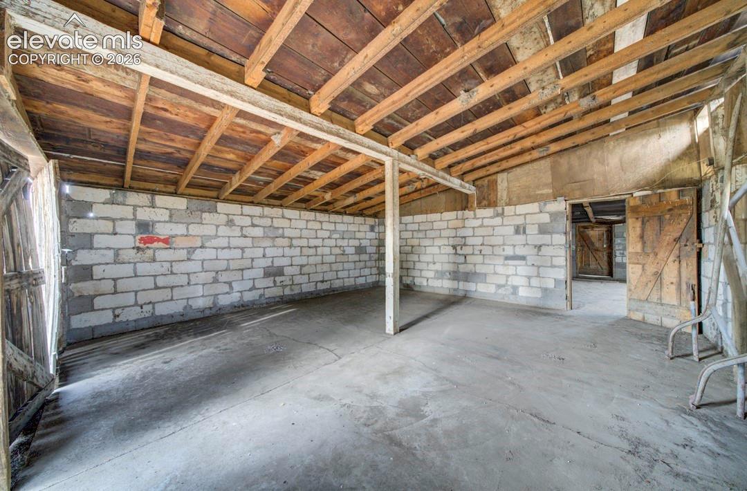 Exposed wood-beam ceiling with wood planking, concrete flooring, and white brick walls