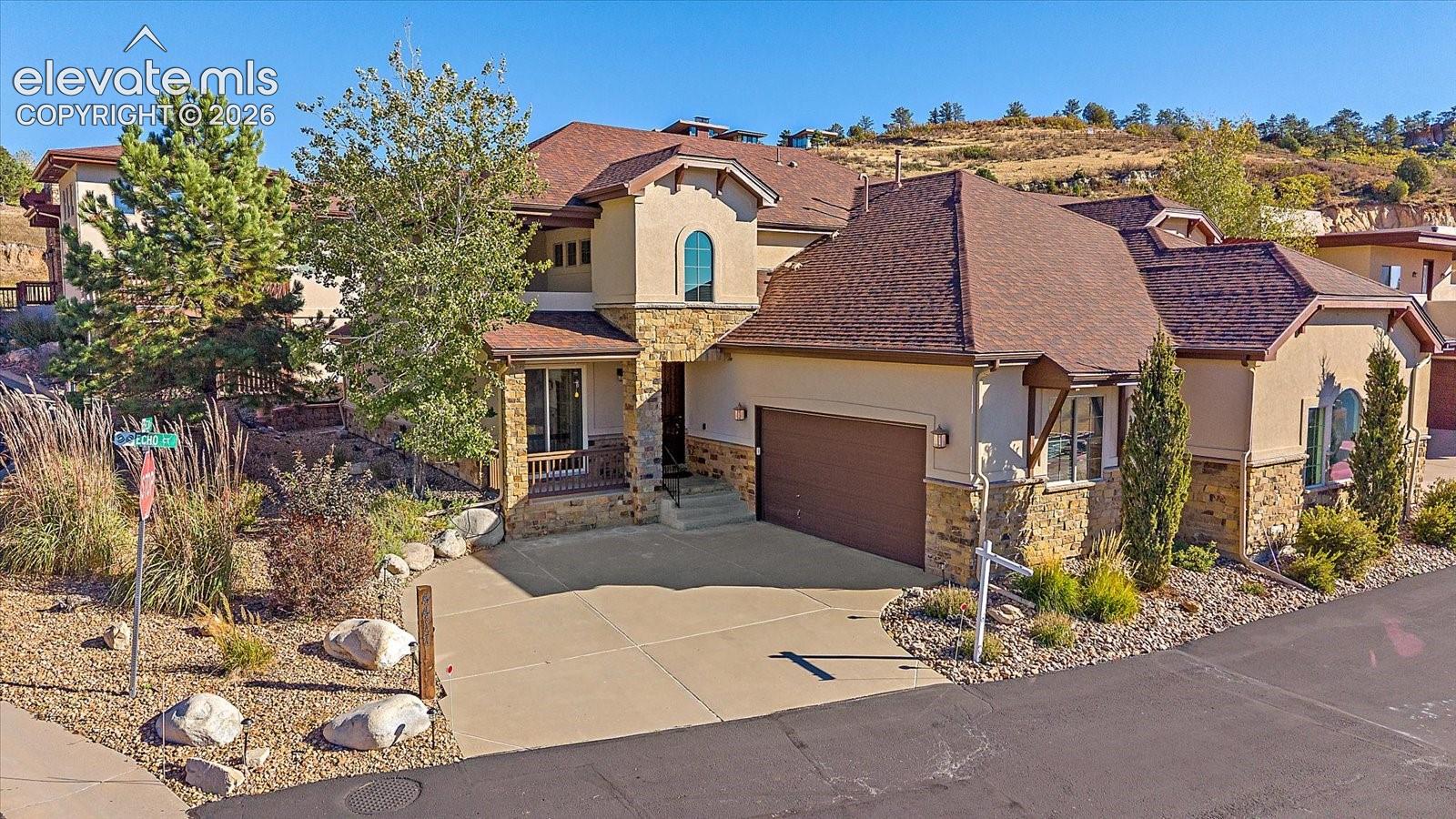 Stucco and stone exterior featuring a multi-gabled roofline, arched window detailing, and a concrete driveway