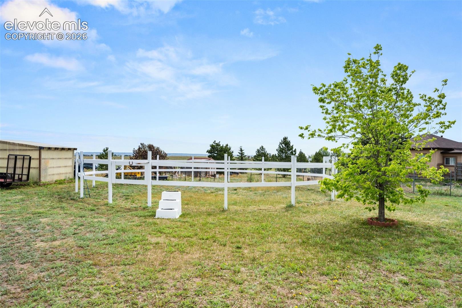 Expansive outdoor area featuring a white perimeter fence, mature foliage, and a detached outbuilding