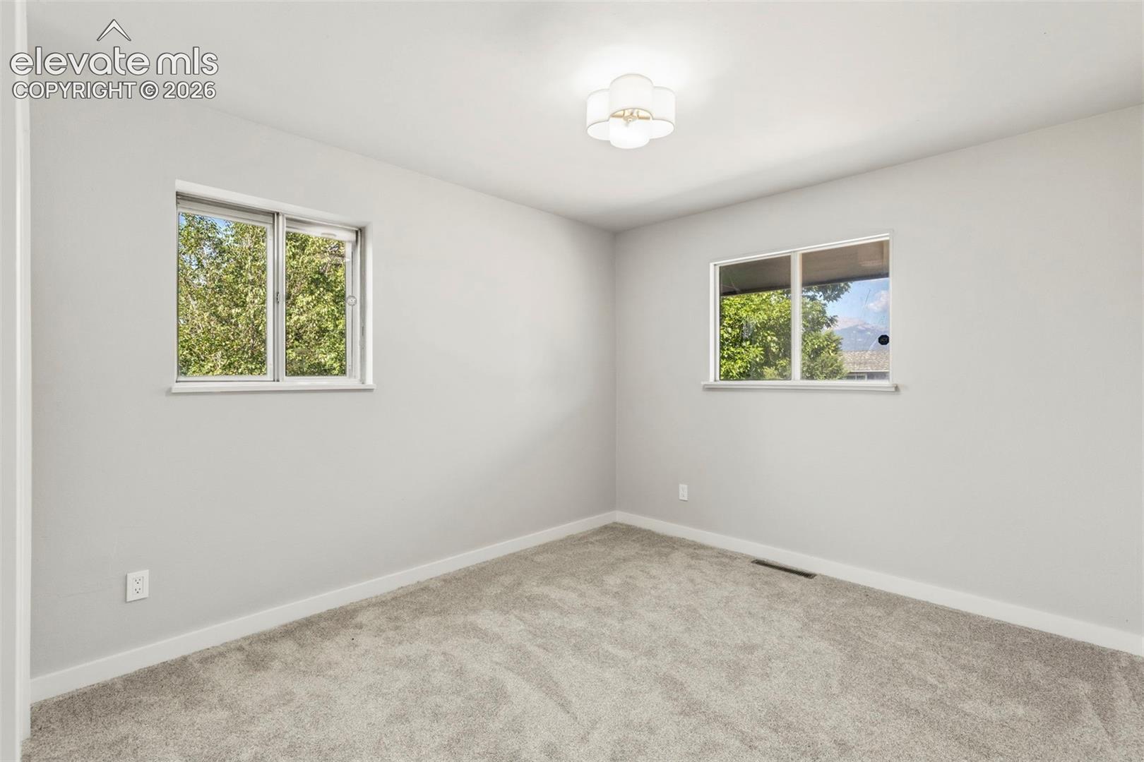 Light taupe carpeted room featuring two windows, a white baseboard, light gray walls, and a decorative ceiling light fixture
