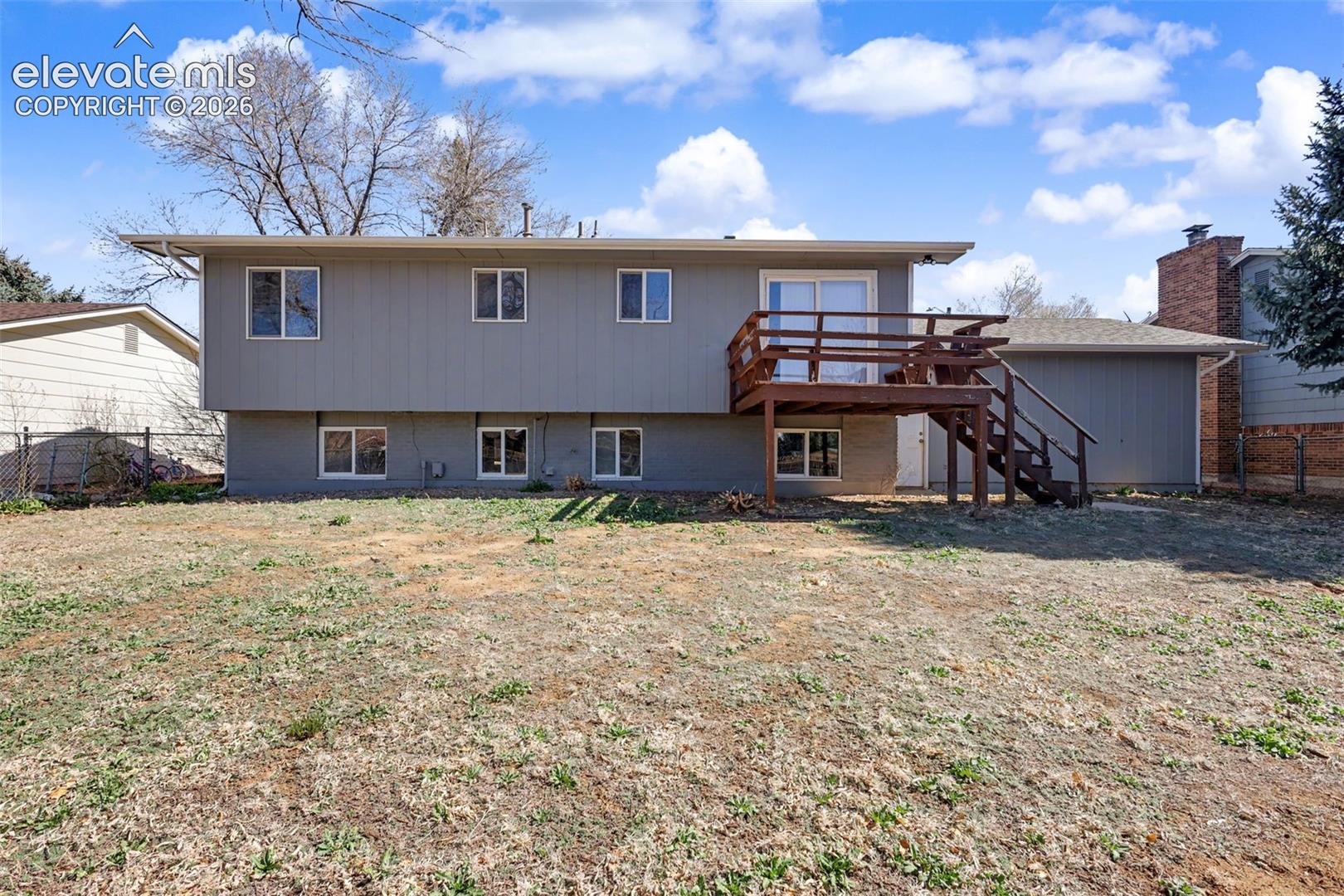 Two-story exterior featuring wood-finish siding, an elevated rear deck with a staircase, and a large backyard area