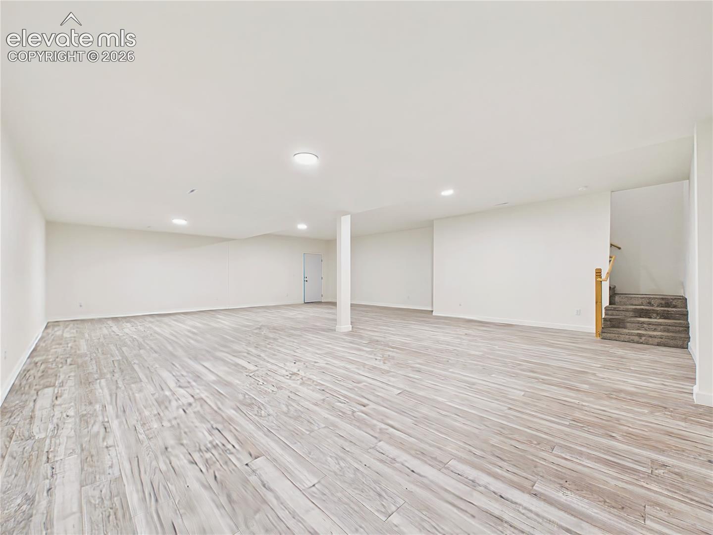 Finished Basement – Wide-angle view emphasizes the scale of the finished lower level, with continuous wood-look flooring, recessed lighting, and an open layout offering numerous possibilities.