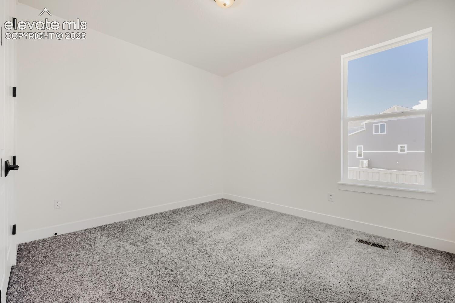 White painted walls, gray patterned carpet, single window with white frame, white trim, and black door hardware