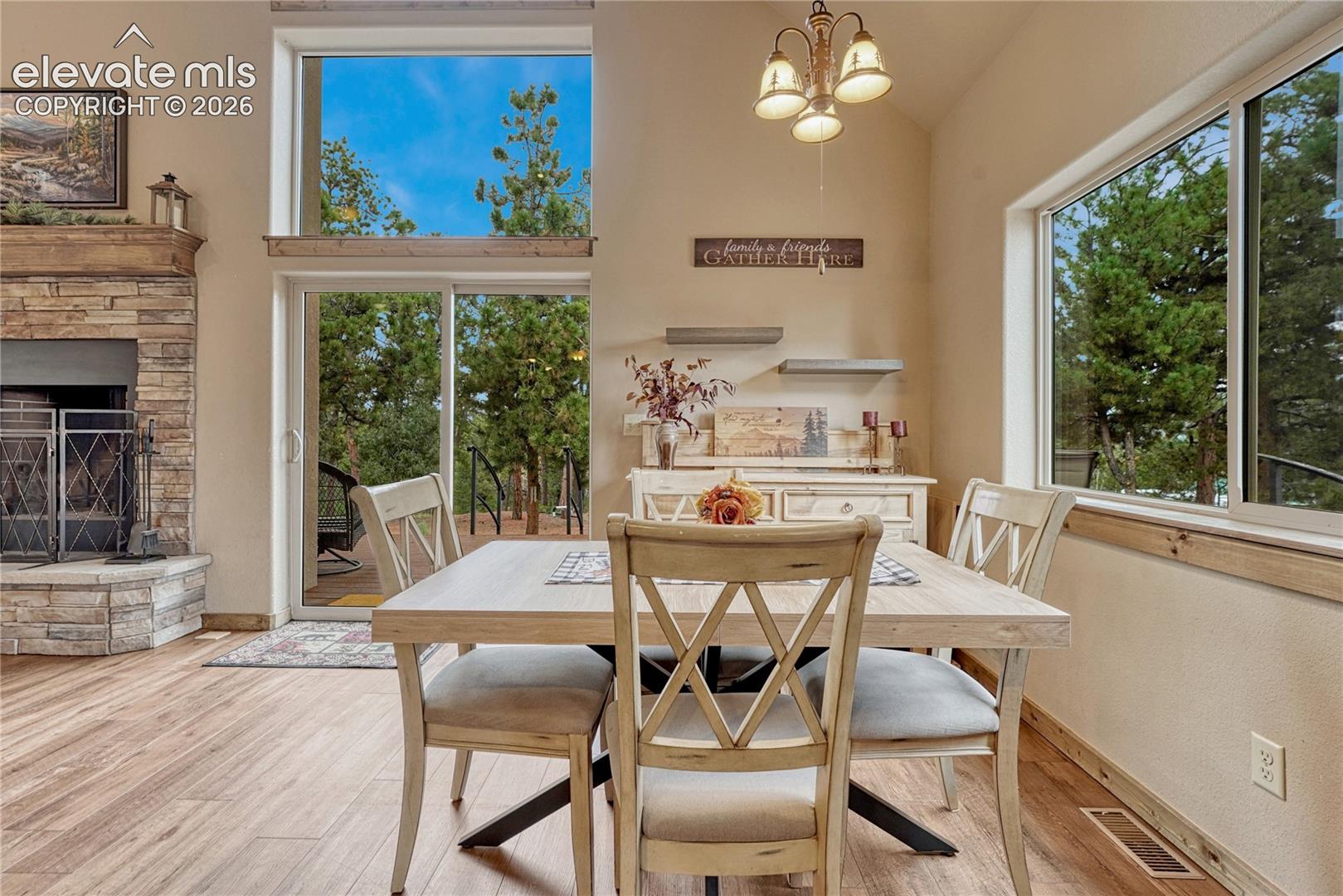 Vaulted ceiling, floor-to-ceiling stone fireplace, wood-finish flooring, sliding glass door with transom window, and expansive picture windows
