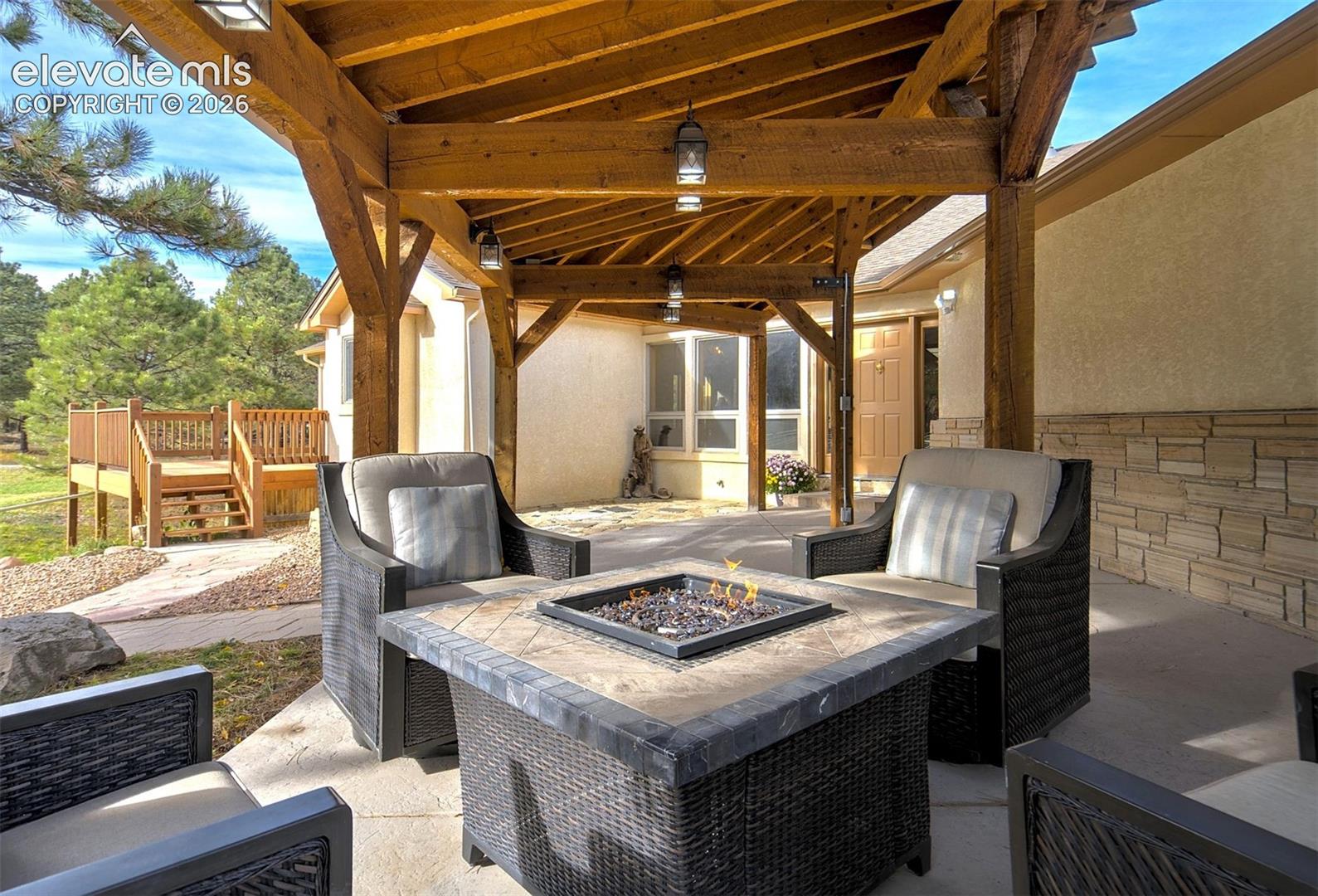 Covered patio featuring a timber-frame pergola, concrete flooring, stone masonry exterior wall, and attached outdoor lighting