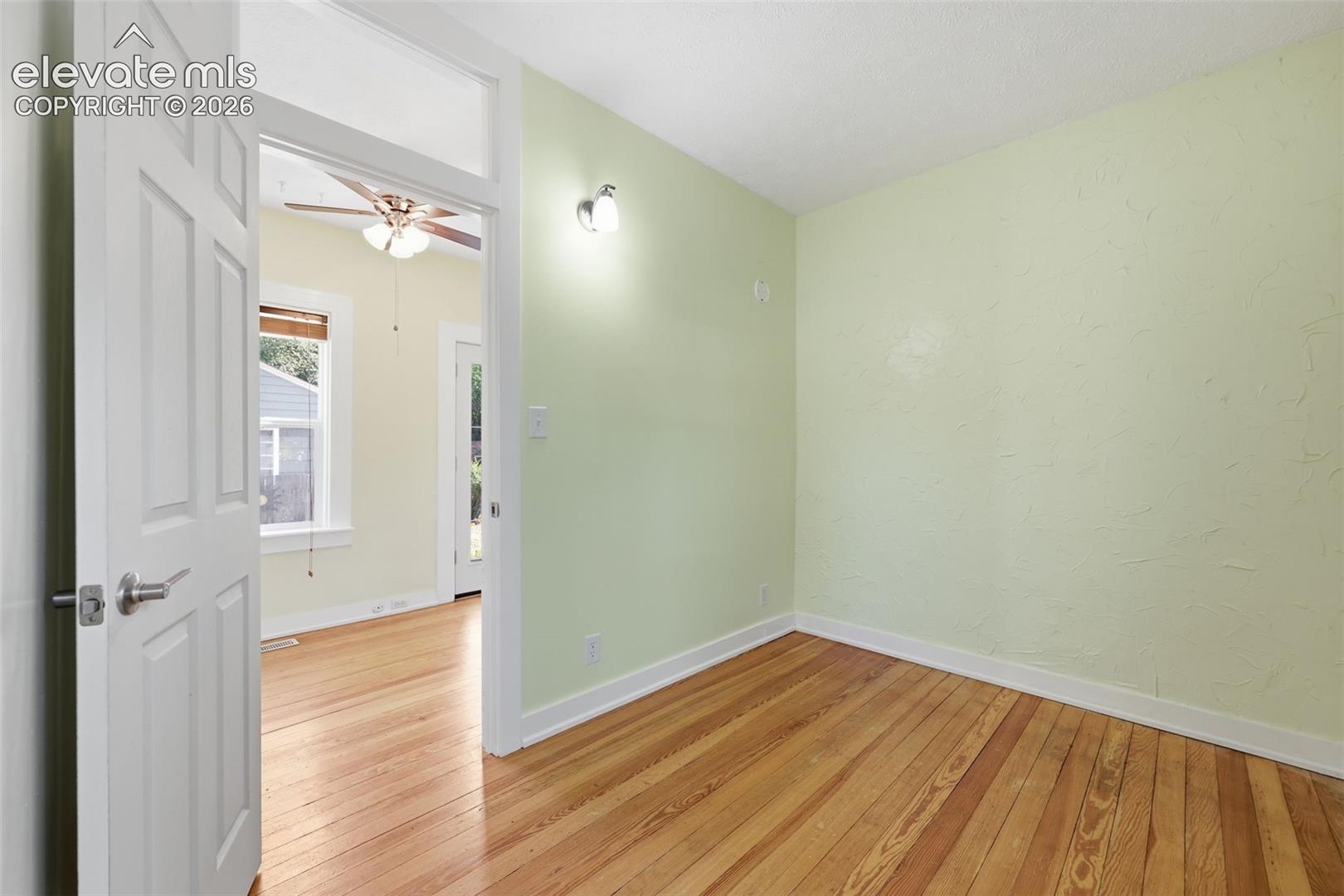 Main-floor bedroom with pine hardwood flooring throughout, white trim, and a wall-mounted light fixture.