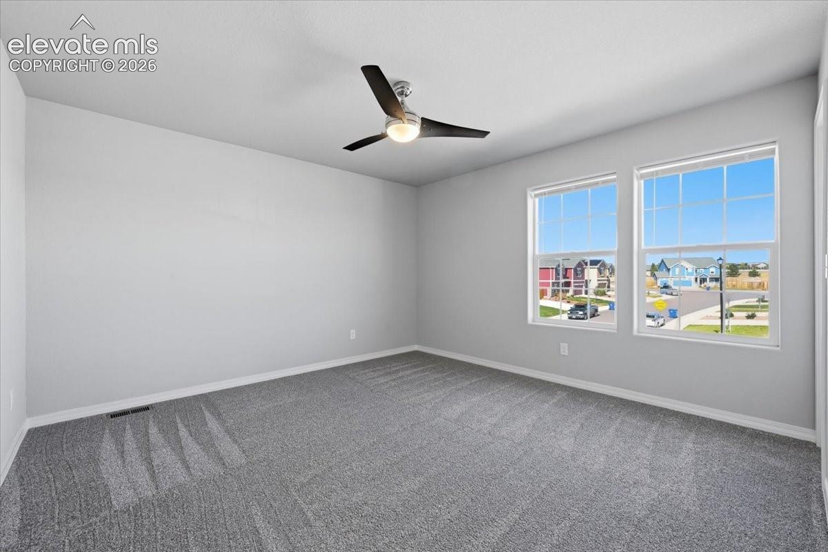 Neutral-toned interior space featuring neutral carpeting, double-hung windows with grid detailing, and a three-blade ceiling fan with integrated lighting
