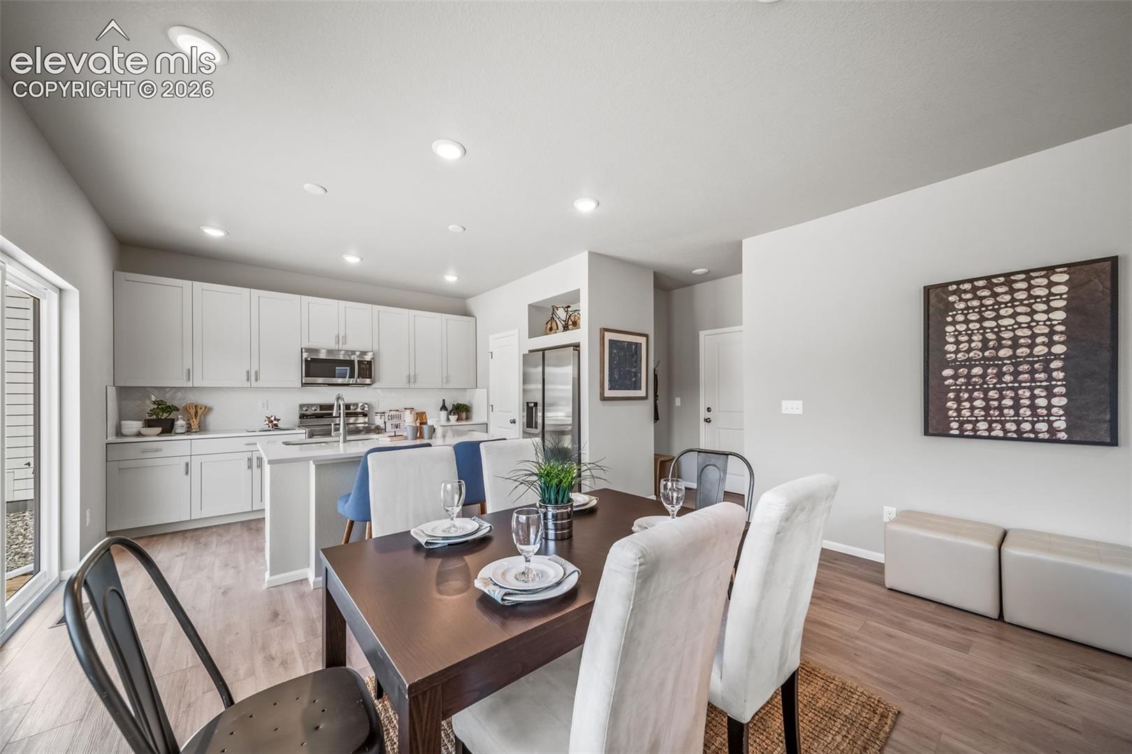 Kitchen and dining area featuring wood-finish flooring, recessed lighting, white shaker-style cabinetry, stainless steel appliances, and a sliding glass door
*photos of a model home*