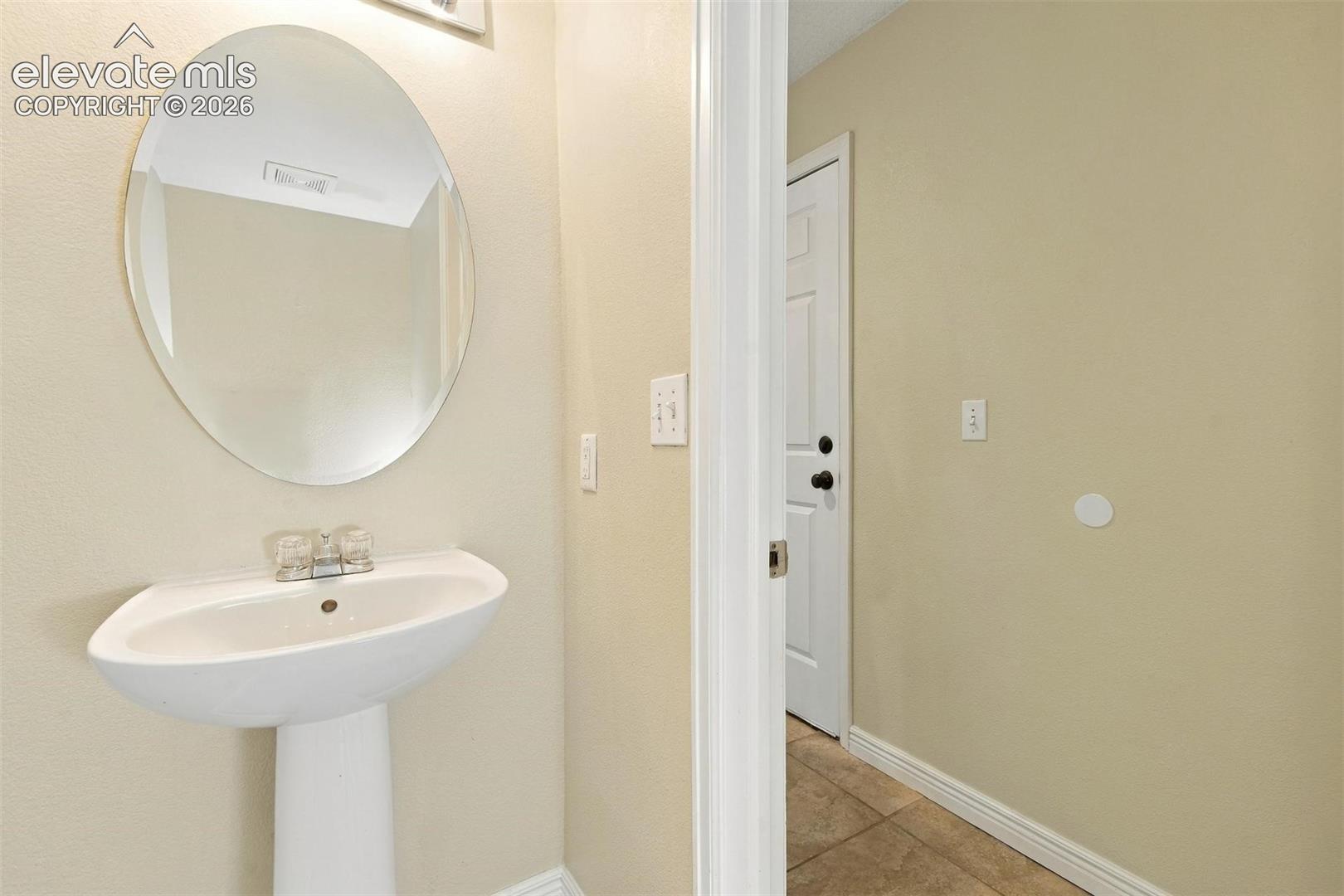 White pedestal sink featuring a chrome dual-handle faucet and oval wall-mounted mirror