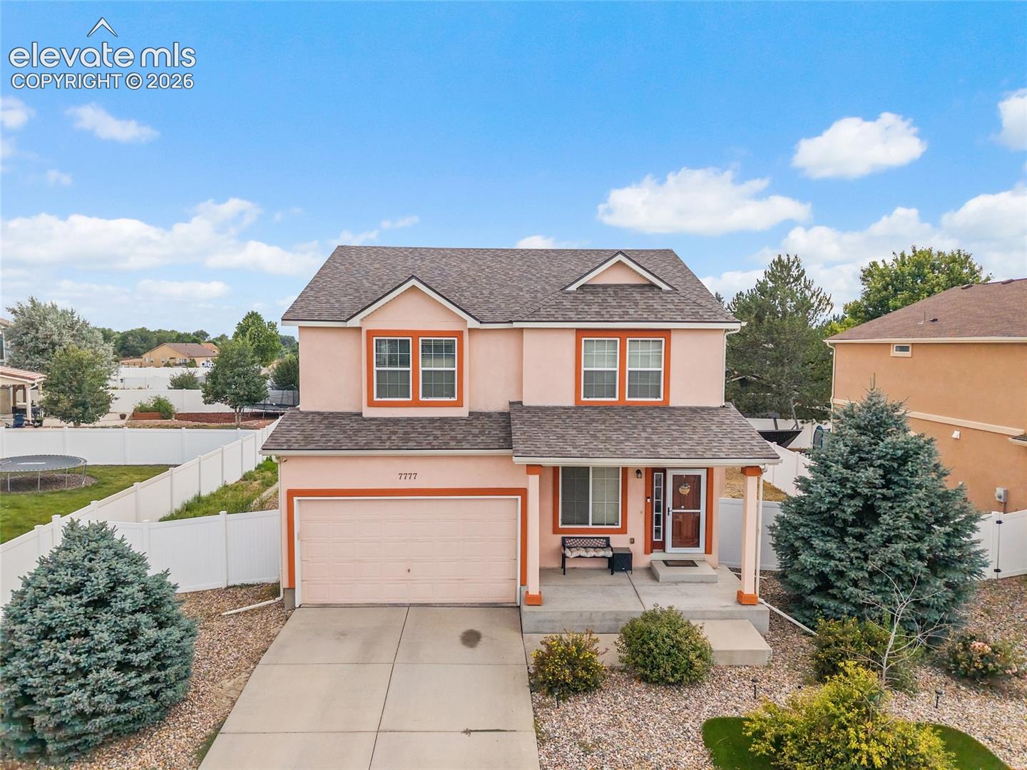 Two-story exterior featuring a concrete driveway, attached garage, covered front porch, and white vinyl privacy fencing