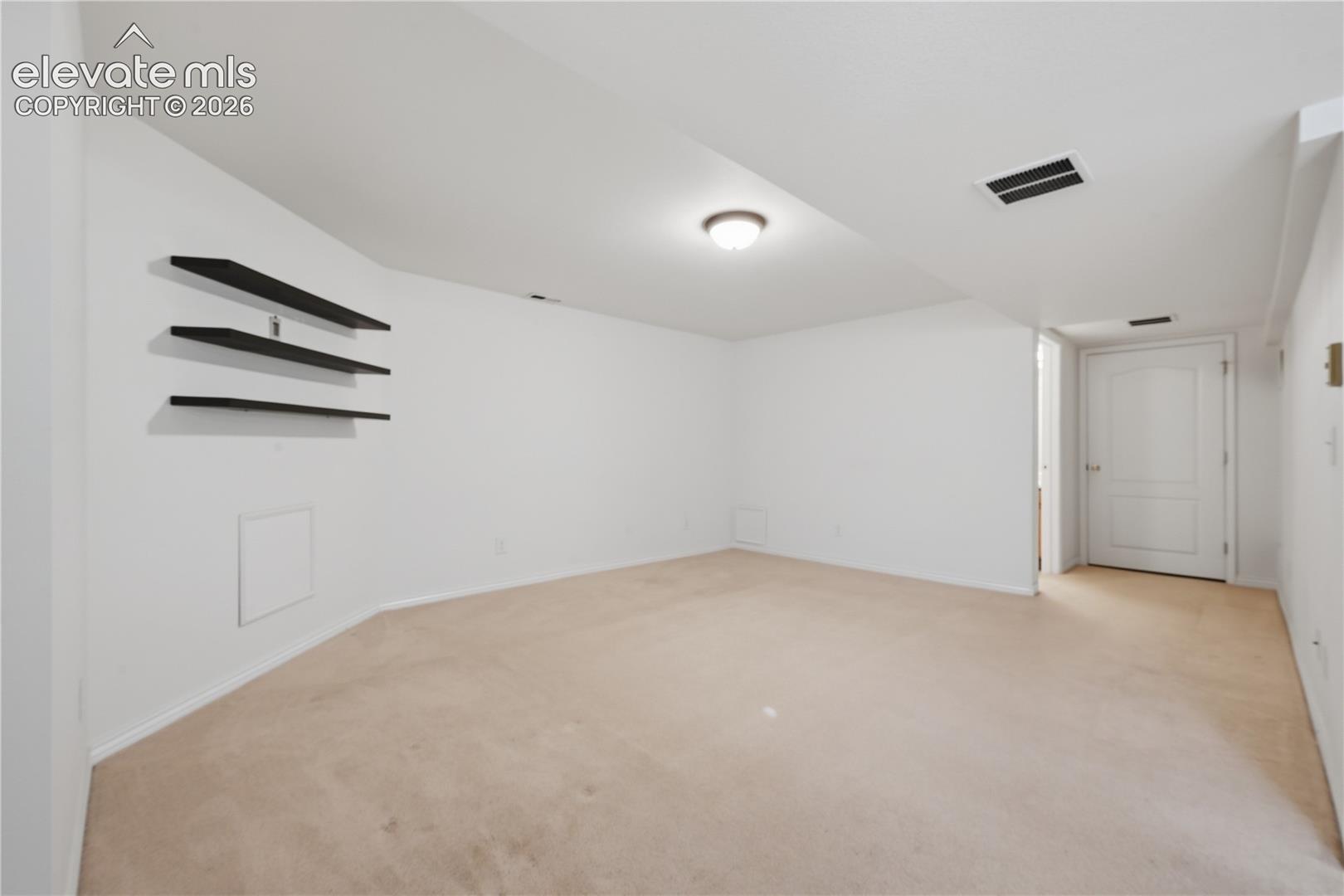 Neutral-toned carpeting, triple-tiered wall-mounted floating shelves, and a solid-panel door