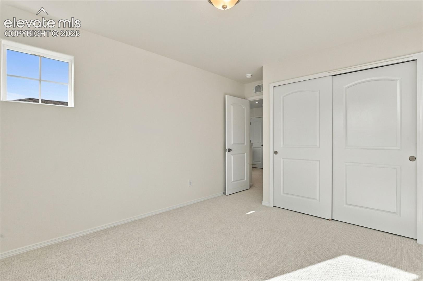 Neutral-toned carpeted flooring, single-pane window with grid muntins, and dual-panel sliding closet doors with matching architectural interior door