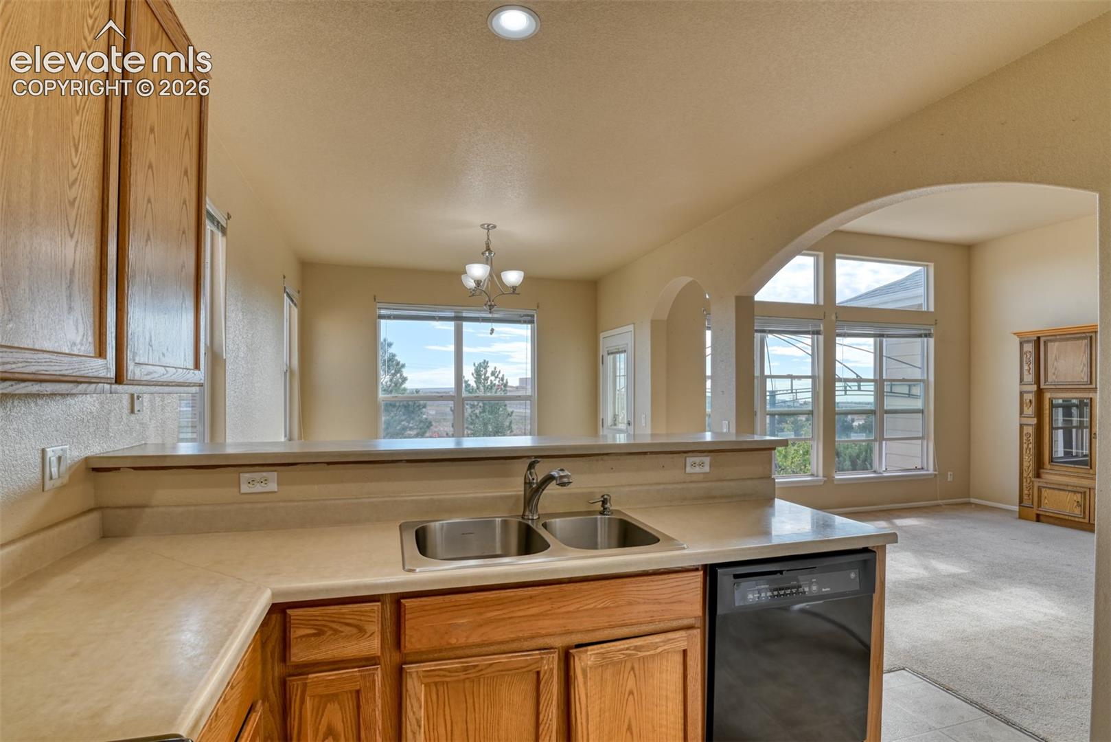 Kitchen featuring solid wood cabinetry, a dual-basin stainless steel sink with a high-arch faucet, a black dishwasher, and expansive windows