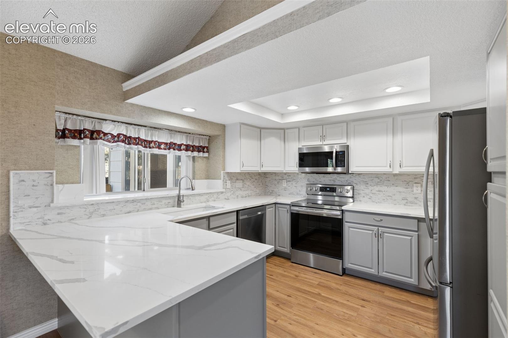 Kitchen featuring a vaulted ceiling, stone-patterned countertops, stainless steel appliances, white and gray cabinetry, and recessed lighting
