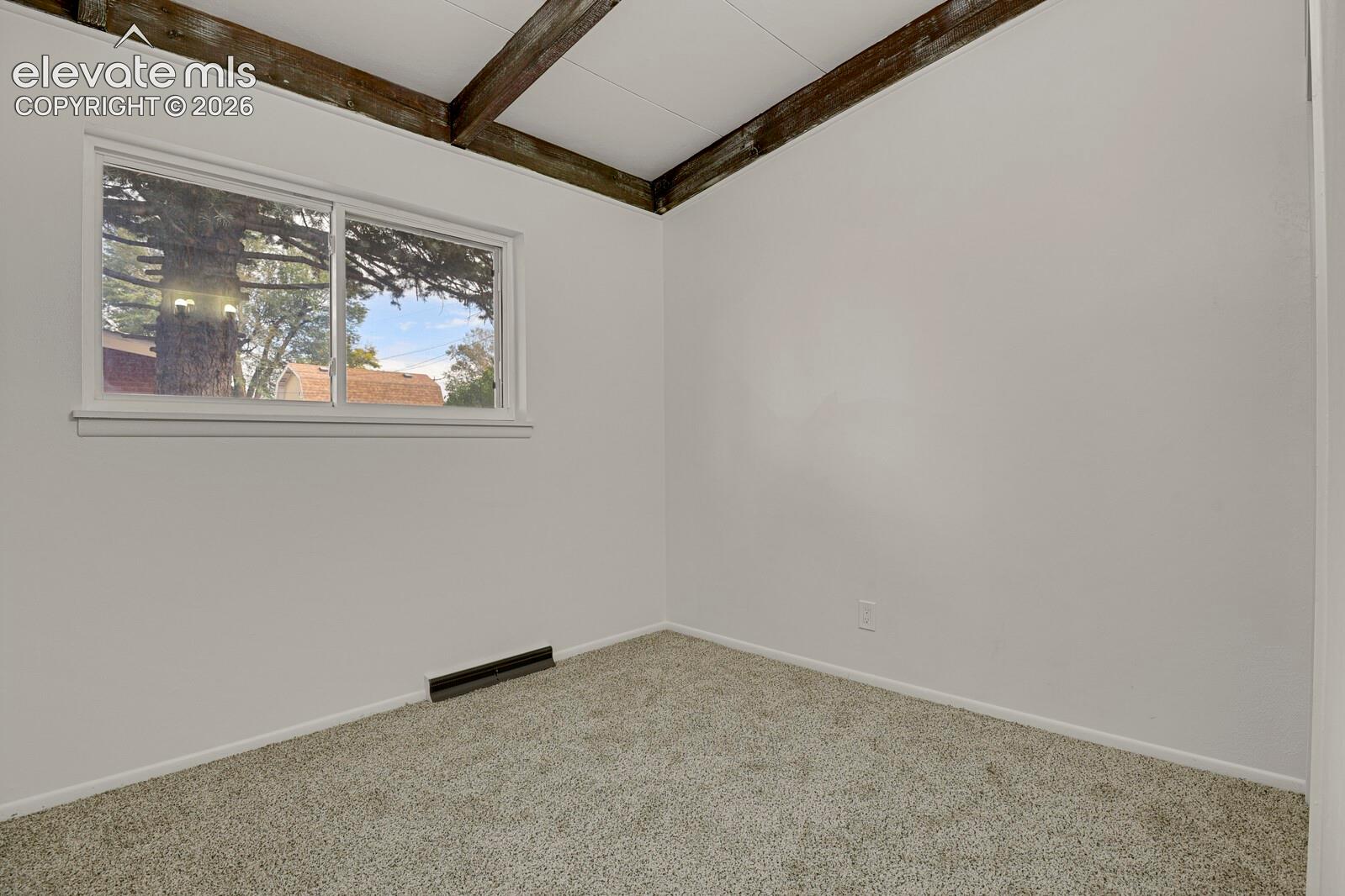 Bedroom featuring exposed wooden ceiling beams, neutral wall paint, carpeting, and a horizontal sliding window