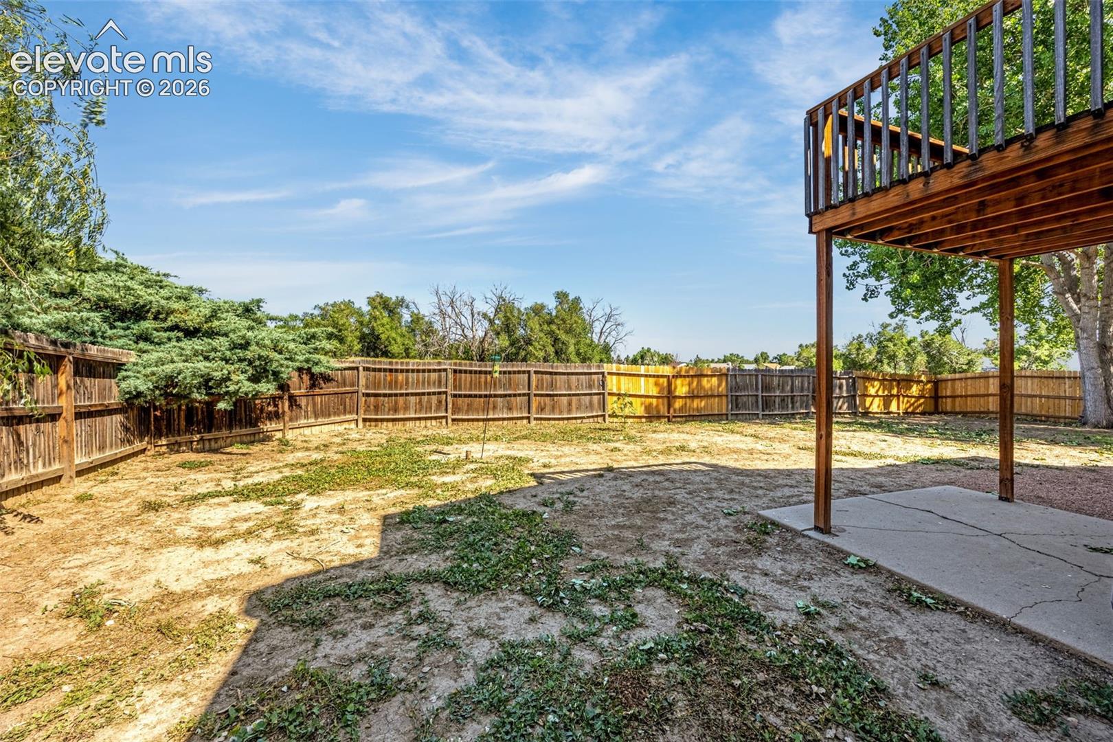 Backyard featuring a wood privacy fence, concrete patio, and elevated wood balcony
