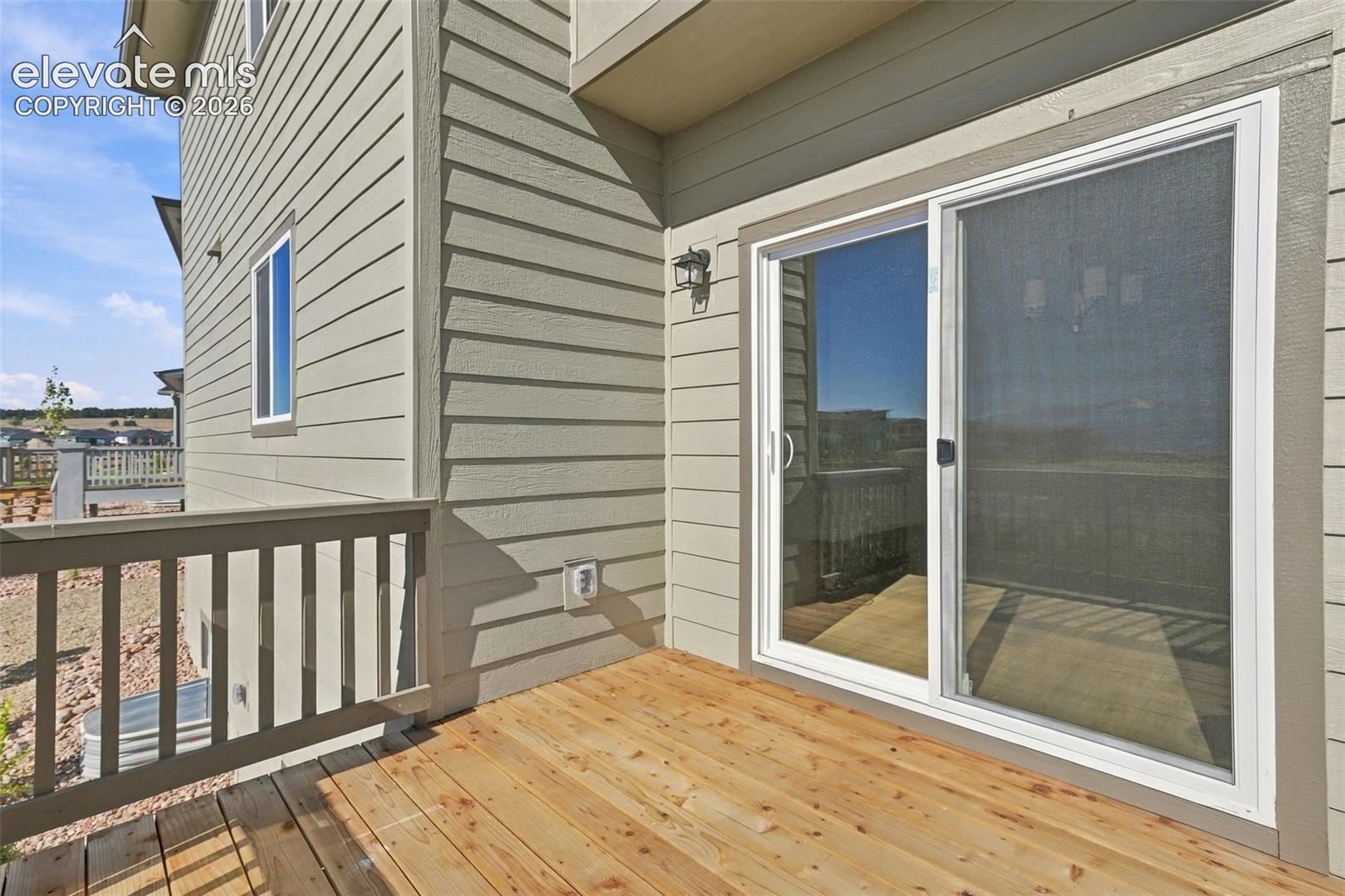 Wood-finish deck with a sliding glass door and wall-mounted exterior lighting