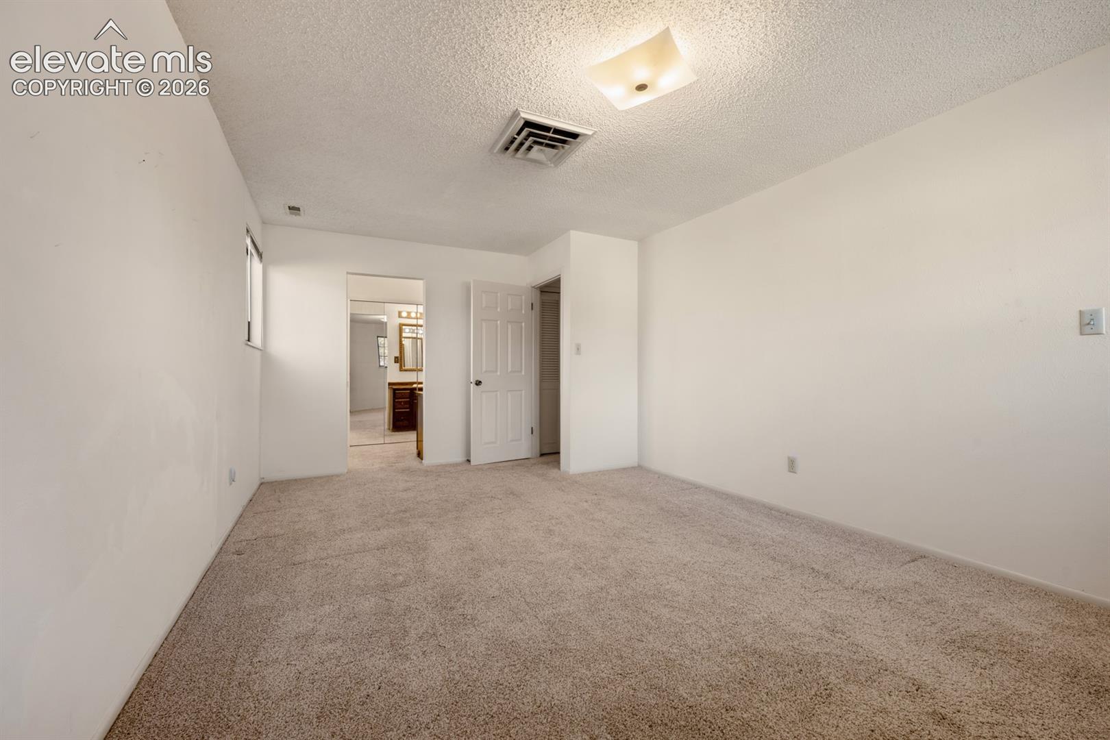 Neutral-toned carpeting, ceiling-mounted square light fixture, and six-panel interior door