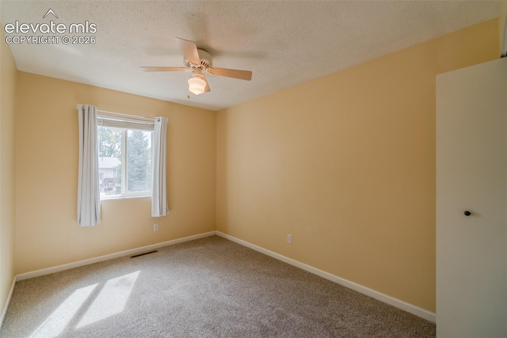 Carpeted room with a ceiling fan, a window with curtains, and a built-in closet