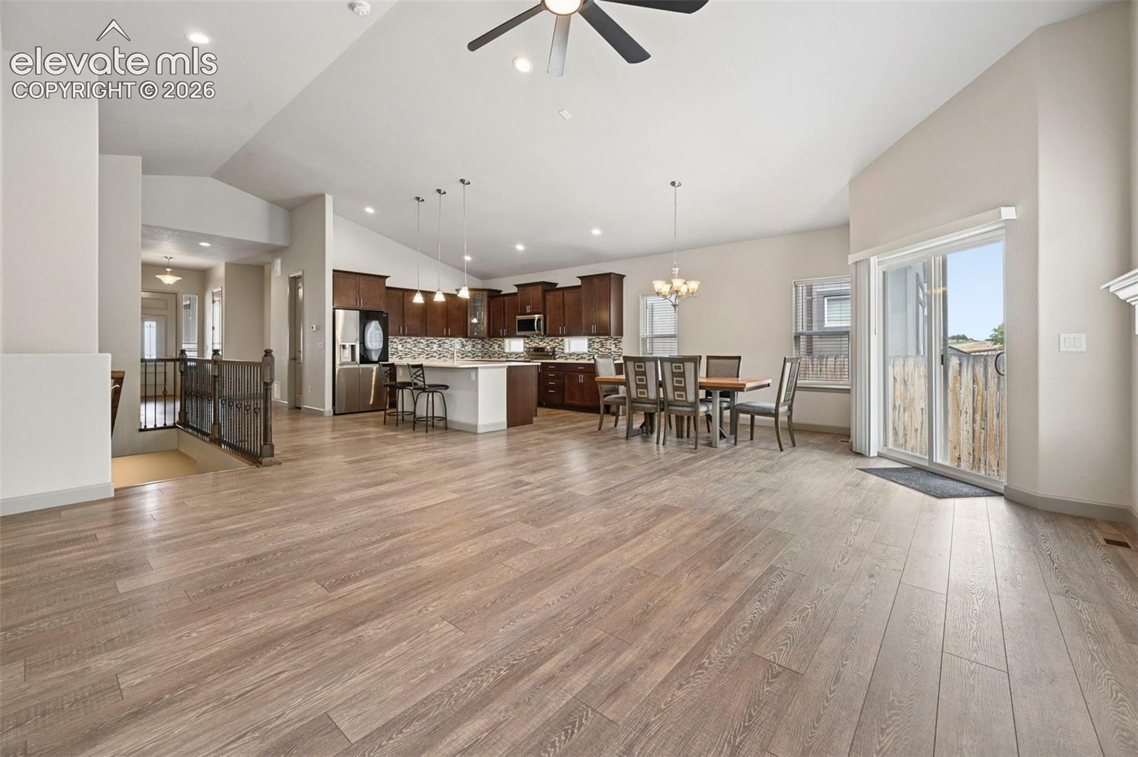 Open-concept area featuring vaulted ceilings, wood-finish flooring, dark wood cabinetry, a center island with pendant lighting, and sliding glass doors