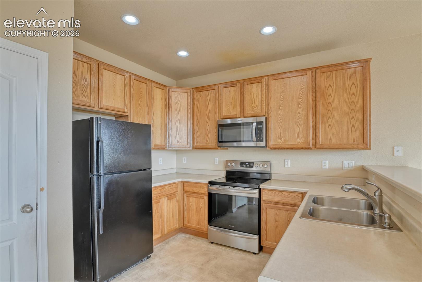 Kitchen featuring natural finish wood cabinetry, stainless steel appliances, dual-basin stainless steel sink with pull-down faucet, and recessed lighting