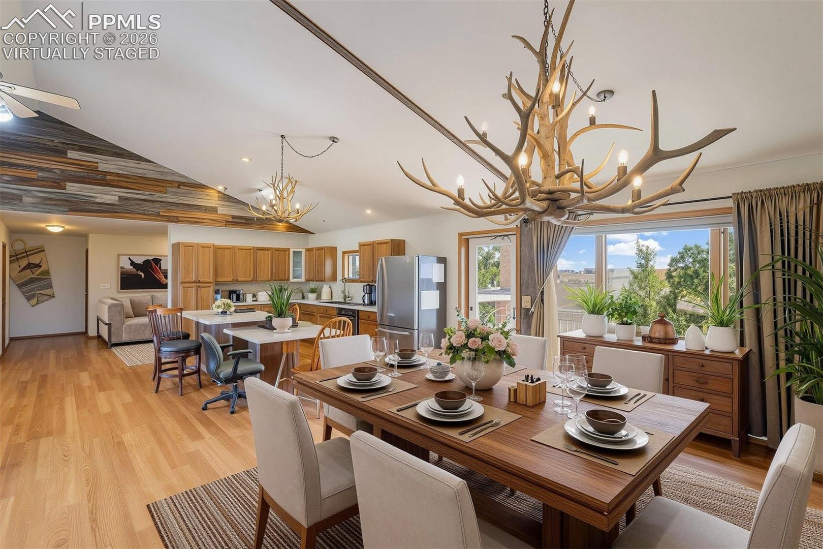 virtually staged Open-concept living space featuring wood-finish flooring, a vaulted ceiling with wood paneling accents, and a kitchen with wood cabinetry and stainless steel appliances