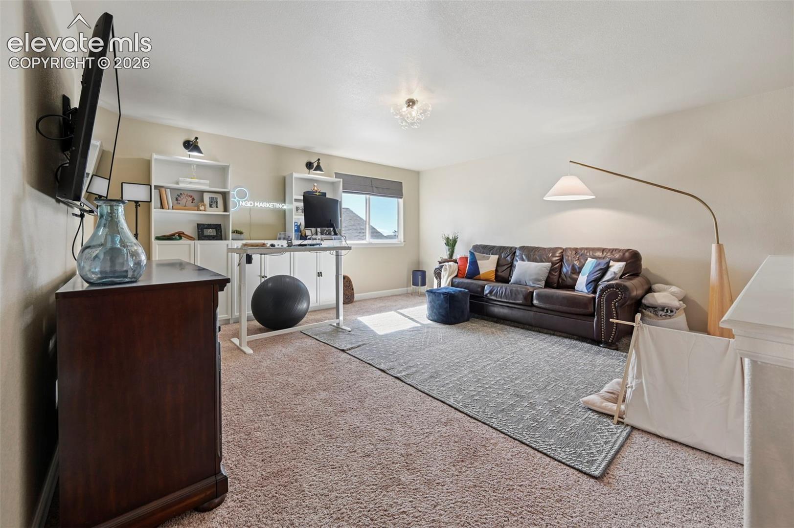 Neutral-toned room featuring wall-to-wall carpeting, built-in white shelving, recessed lighting, and a window with a roman shade