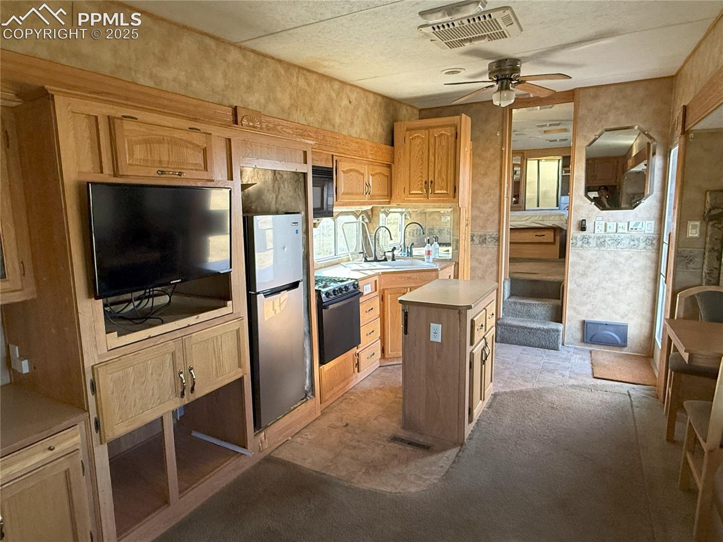 Kitchen featuring light countertops, freestanding refrigerator, a ceiling fan, light brown cabinets, and a kitchen island