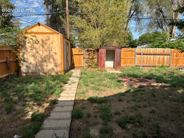 Expansive backyard featuring a paver pathway, wood privacy fencing, a large wood-sided storage shed, and a smaller metal shed