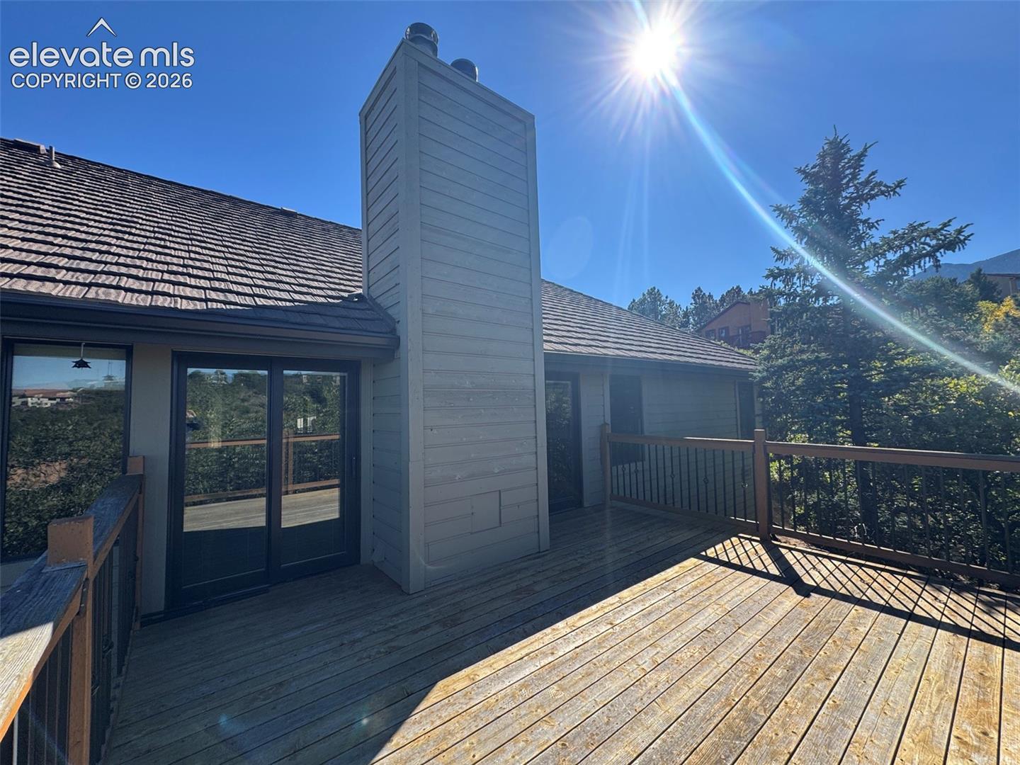 Spacious wood deck featuring an exterior chimney, sliding glass doors, and a wood railing