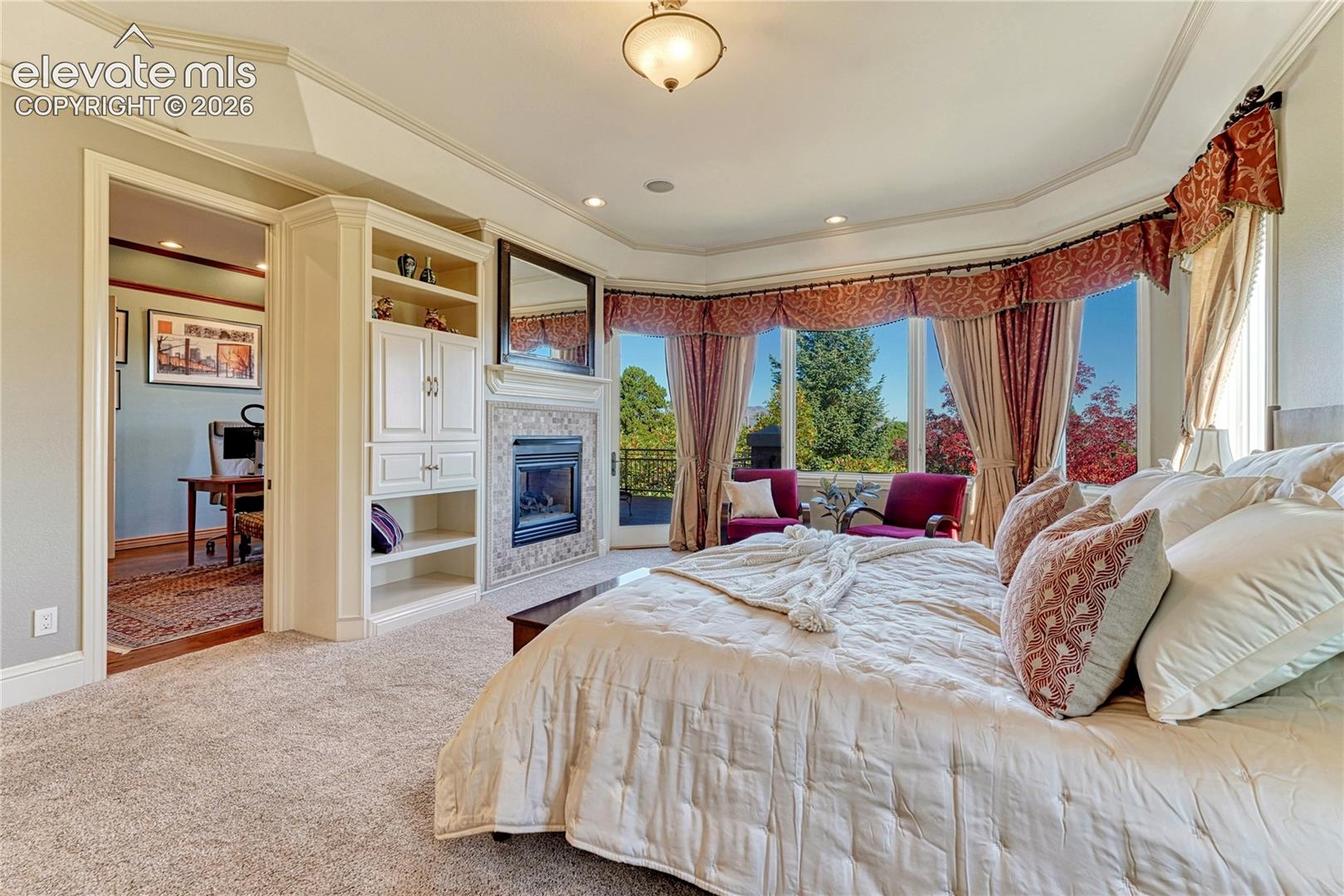 Bay window with multi-panel glass, fireplace featuring tile surround and mantle, built-in cabinetry, tray ceiling, and recessed lighting