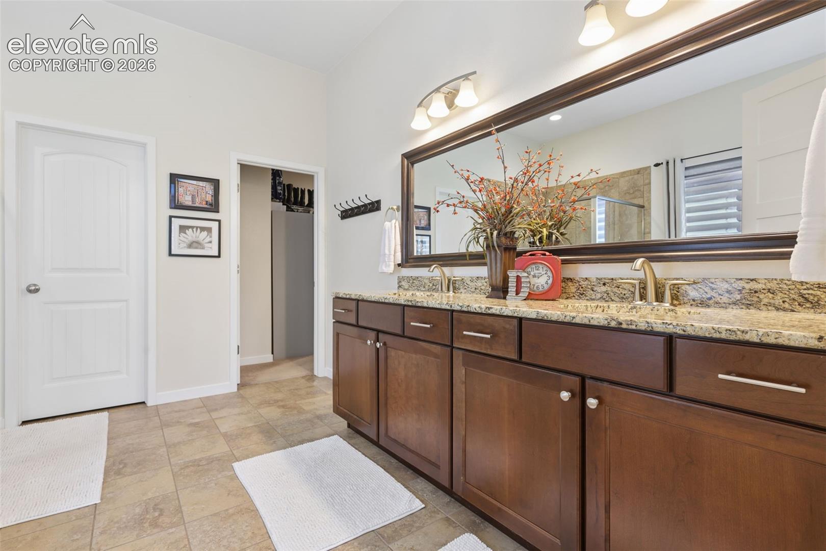 Spa-inspired primary bathroom featuring a dual-sink vanity with wood cabinetry, granite countertops, and an expansive framed mirror