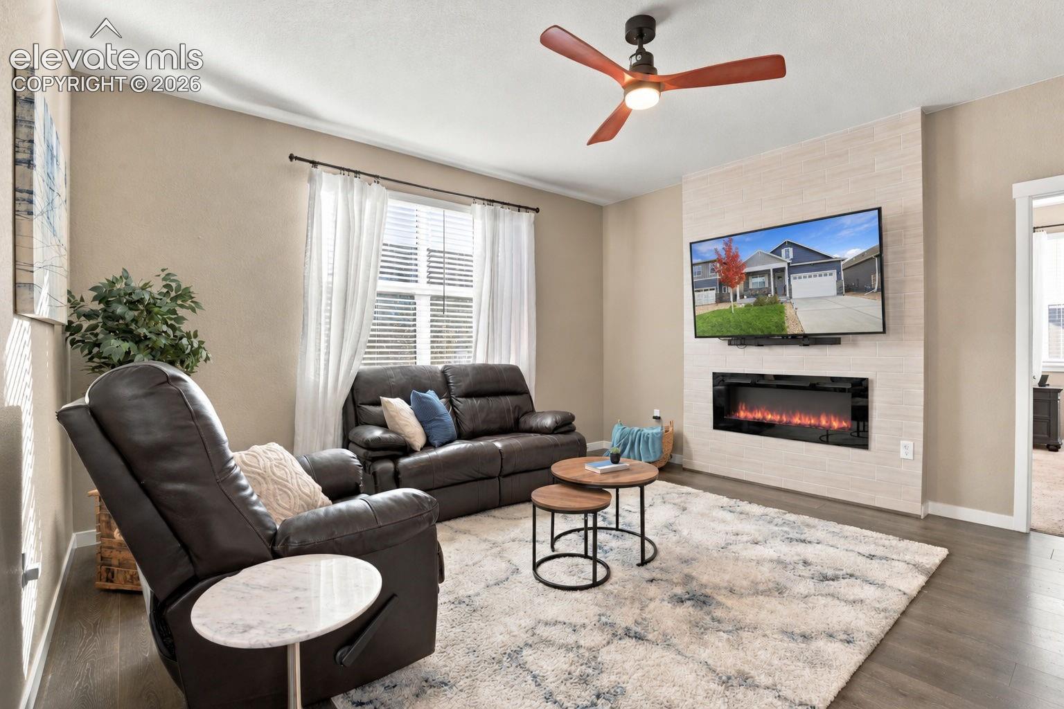 Living area featuring a modern linear electric fireplace, full-height tile accent wall, wood-finish flooring, and a contemporary ceiling fan