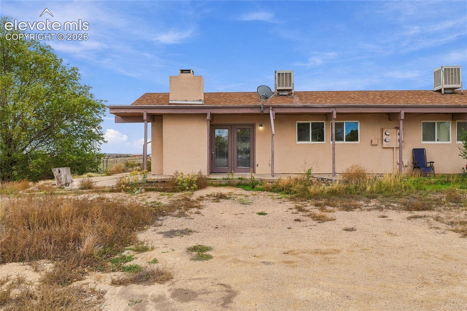 Single-story exterior featuring a stucco finish, shingle roof, chimney, covered patio, and glass-paneled double doors