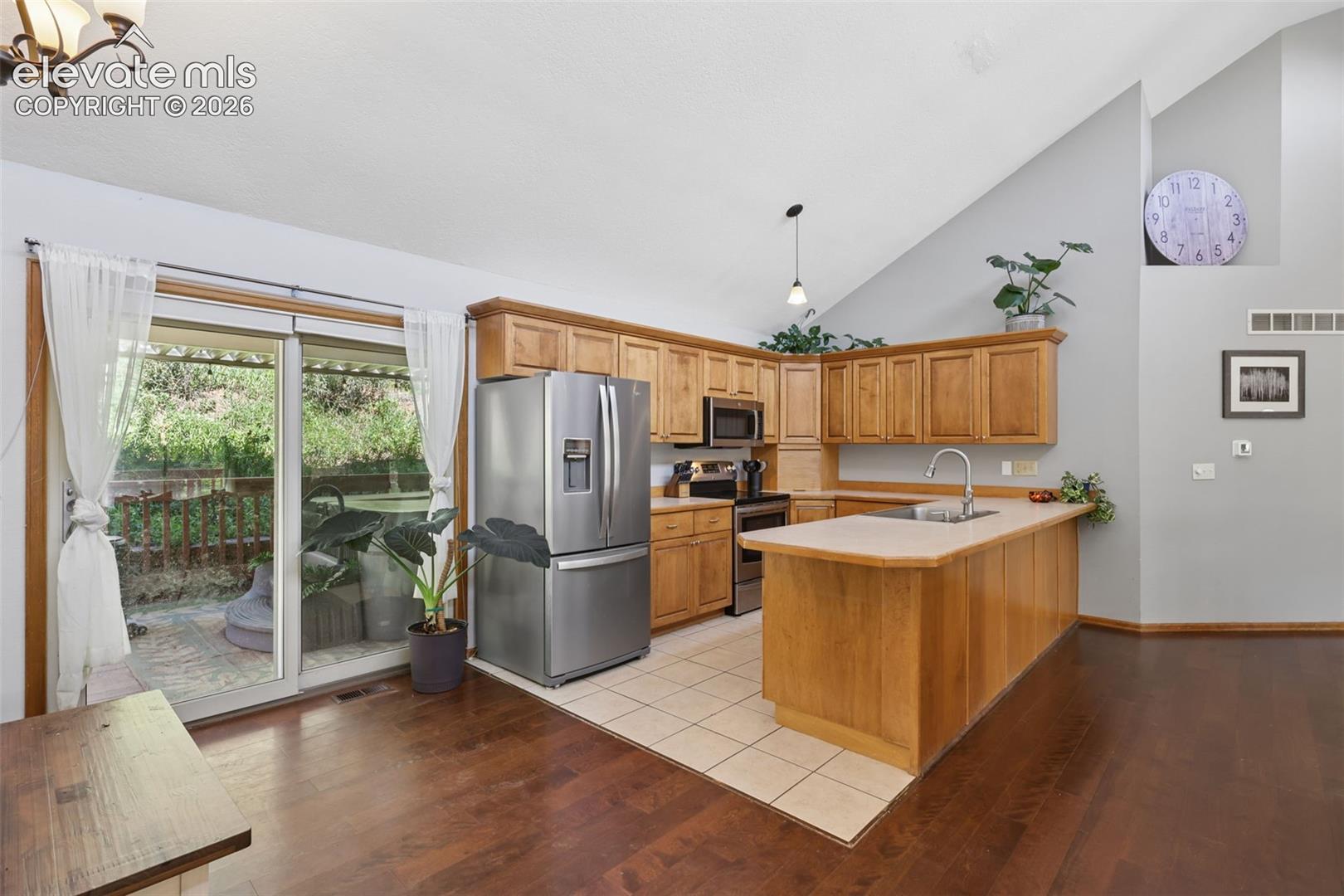 Vaulted ceiling, wood-finish flooring, stainless steel appliances, sliding glass doors, and a kitchen island with integrated sink