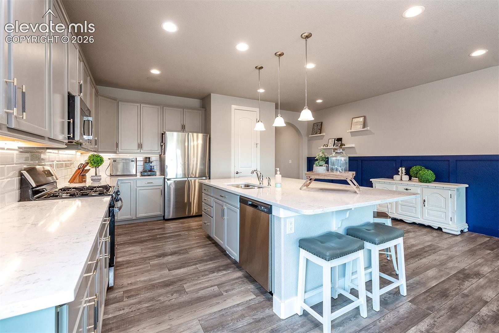 Modern kitchen featuring  wood laminate flooring, stainless steel appliances, recessed lighting, a large center island with pendant lighting, and a subway tile backsplash
