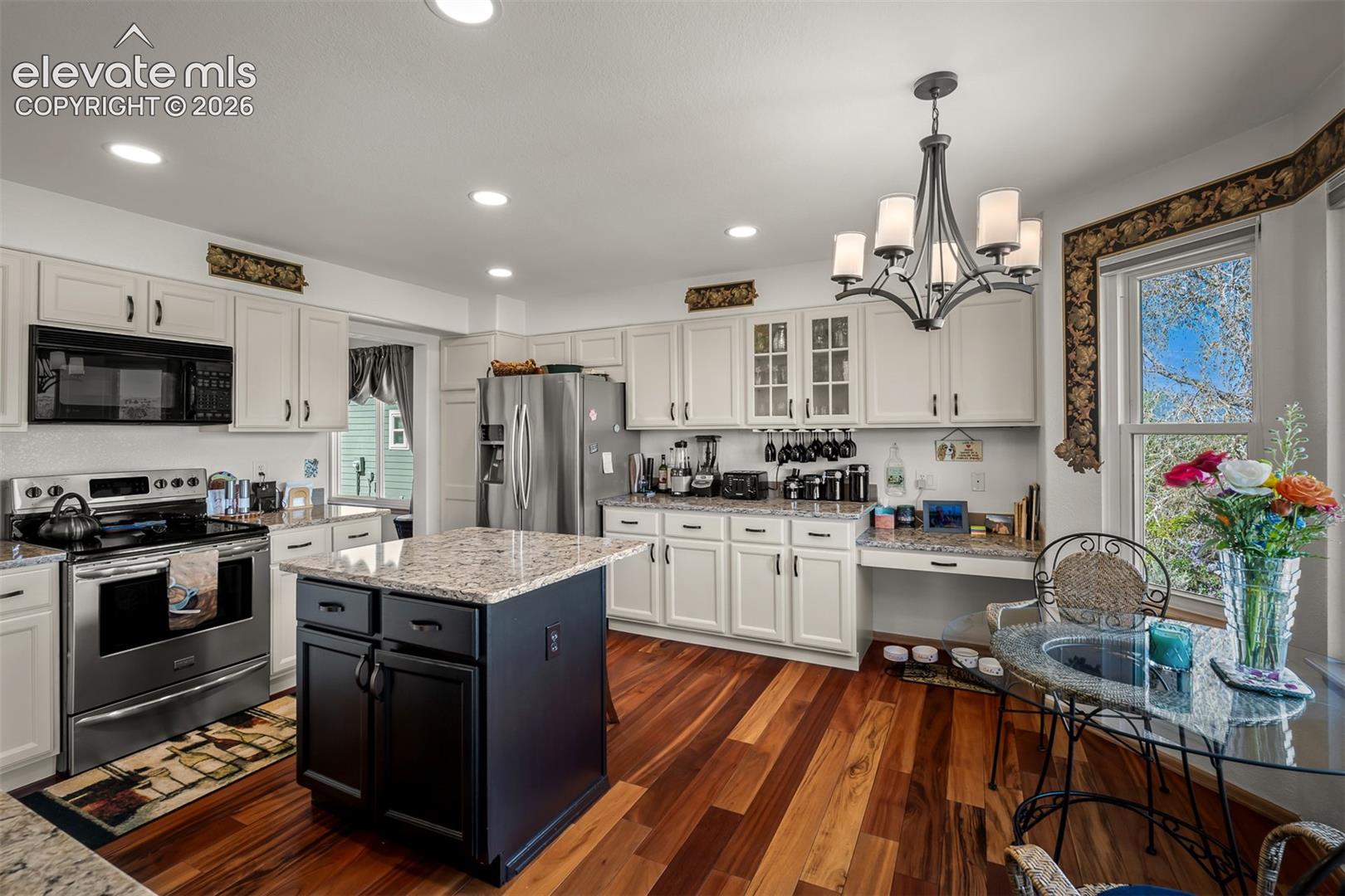 Kitchen featuring Brazilian Koa hardwood flooring, white cabinetry, granite countertops, stainless steel appliances, and a central island with quartz countertops.