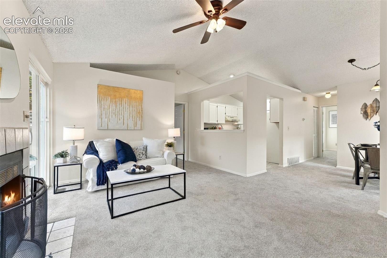 Living area featuring vaulted ceilings, a fireplace with a tile surround, a ceiling fan with integrated lighting, and neutral carpeting