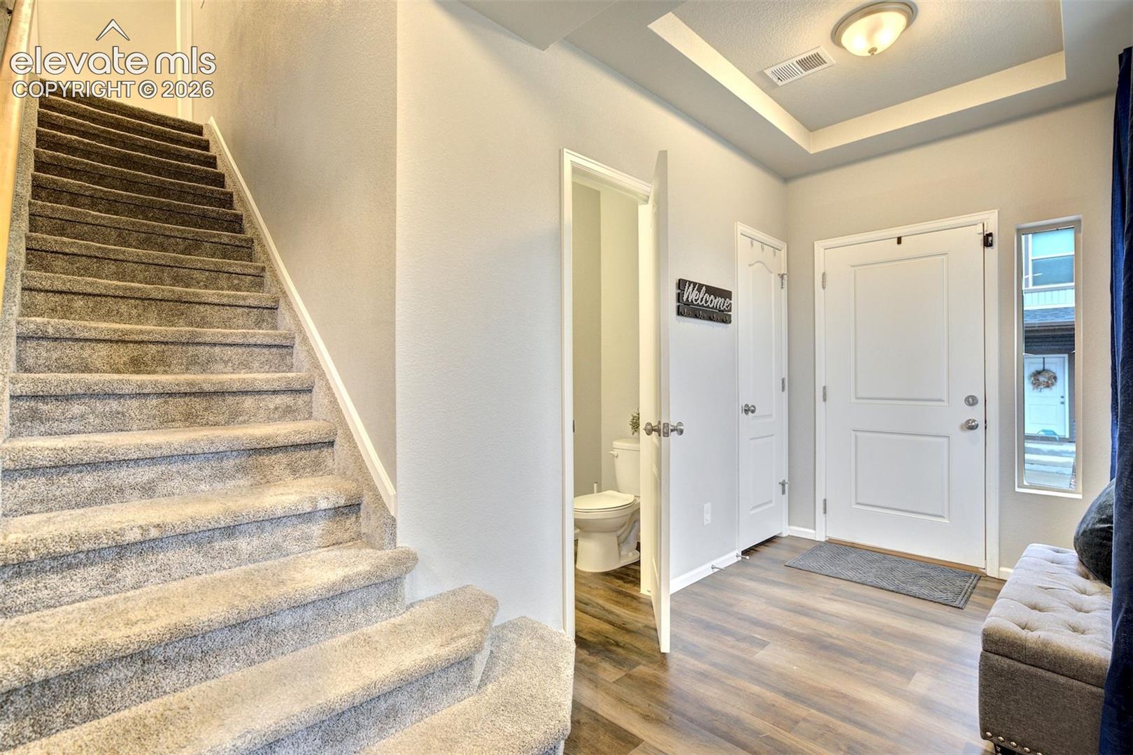 Entryway featuring wood-finish flooring, carpeted stairs, a tray ceiling with recessed lighting, and a paneled entry door with a sidelight