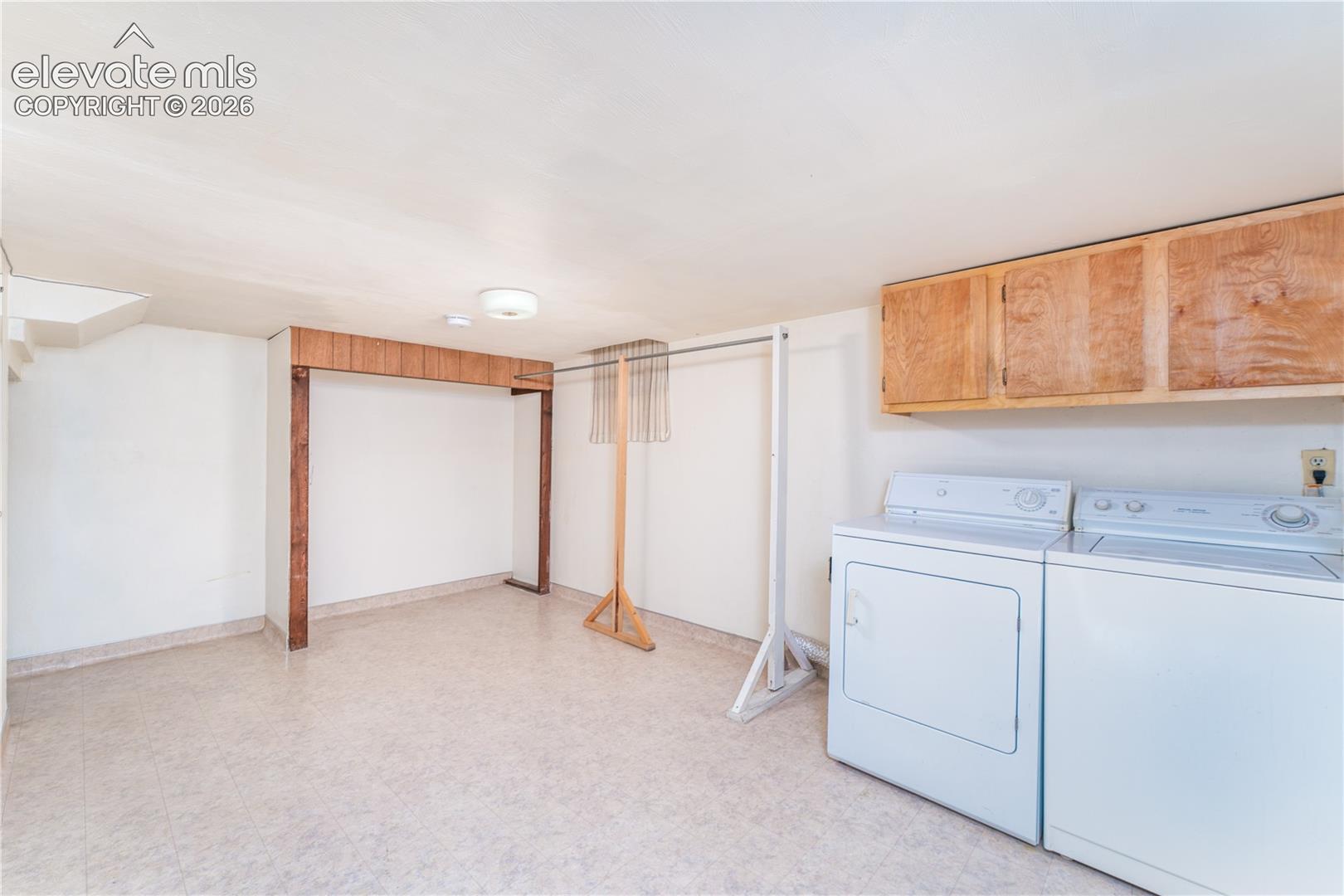 Dedicated laundry space with light-toned flooring, overhead wood-finish cabinetry, and a ceiling-mounted light fixture