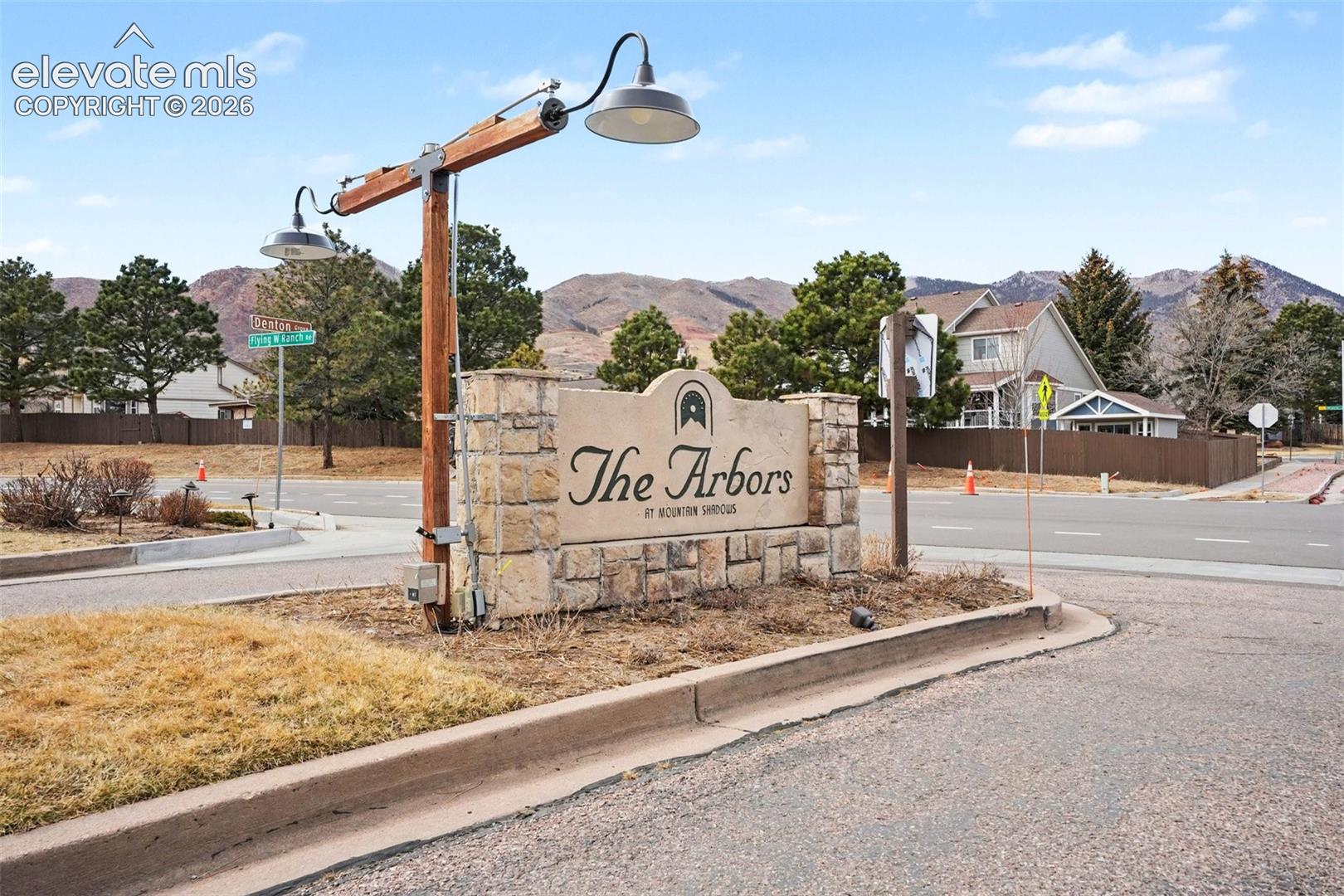 Community entrance monument featuring stacked stone masonry, custom architectural signage, and dual gooseneck industrial-style lighting