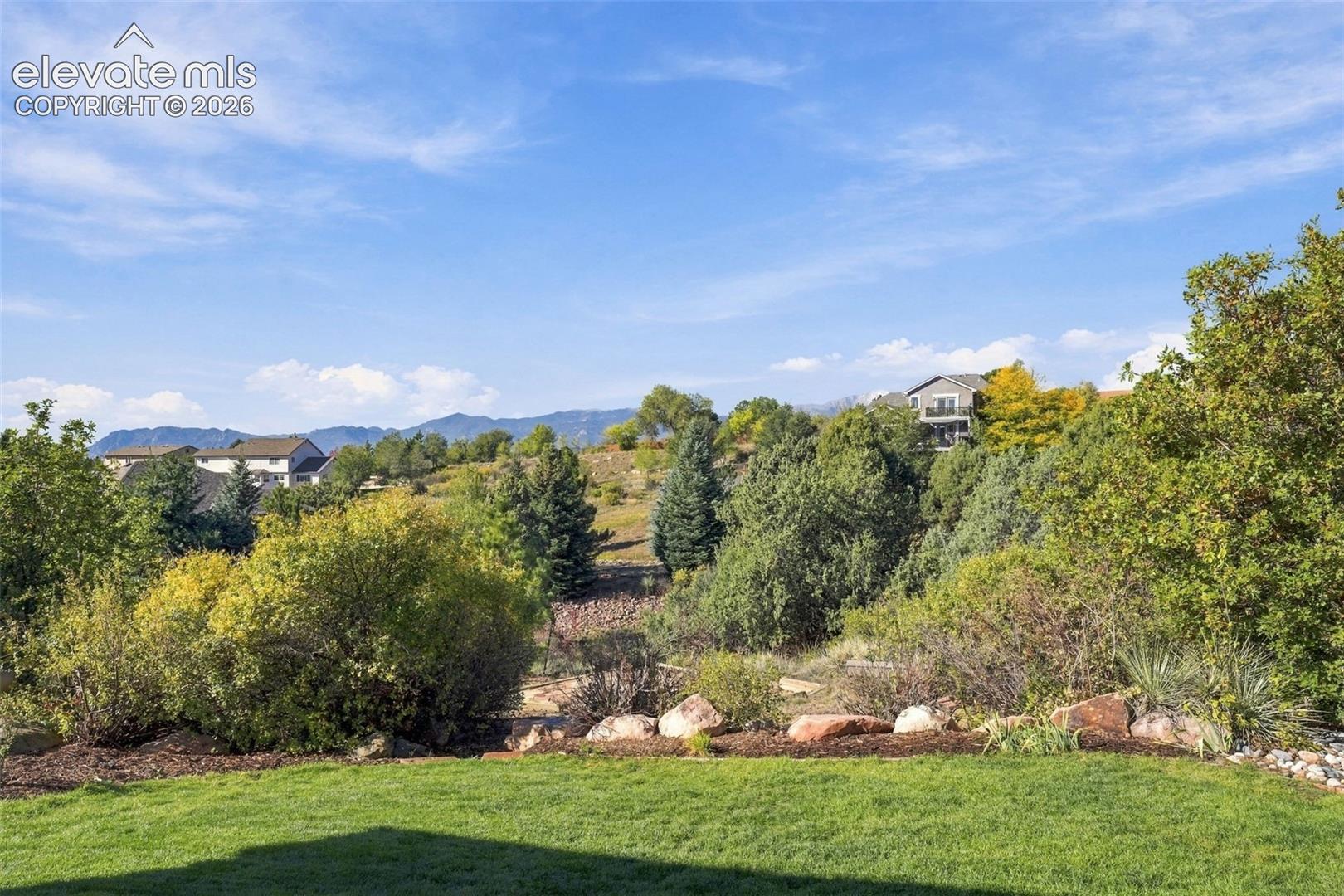 Outdoor space featuring a manicured lawn, natural boulder accents, mature evergreen and deciduous trees, and a mountain backdrop