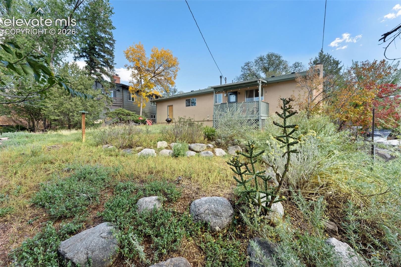 Exterior stucco finish, rear balcony, and sloped natural landscaping with rocks
