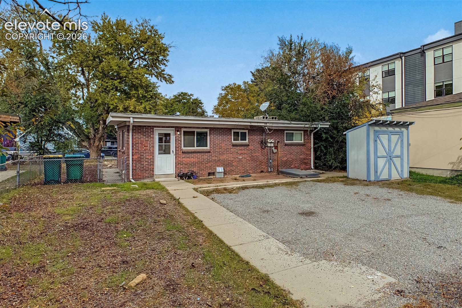 Brick exterior siding, concrete walkway, detached storage structure, and gravel parking area