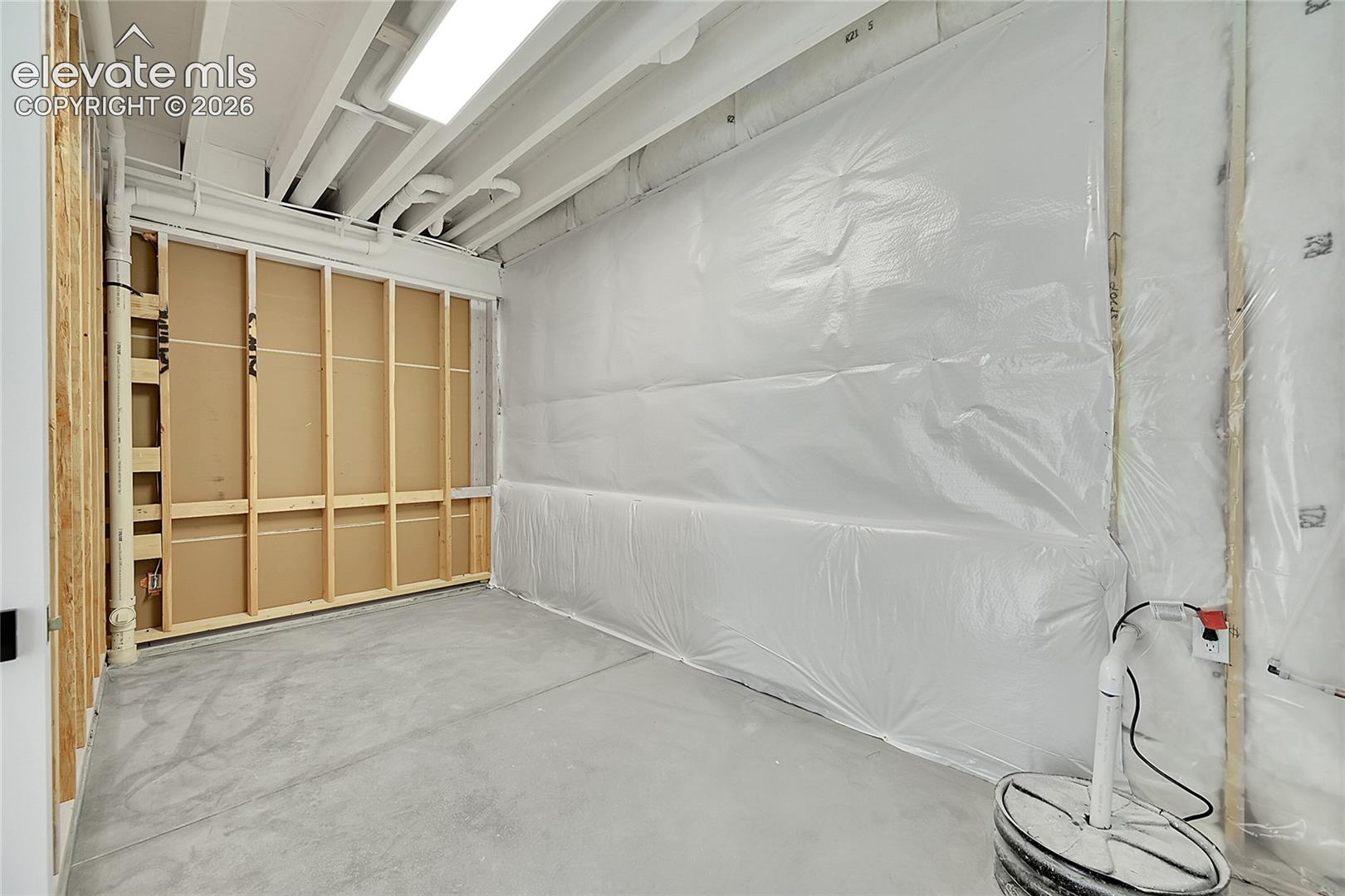 Unfinished basement space featuring exposed wood framing, concrete flooring, and ceiling-mounted fluorescent lighting