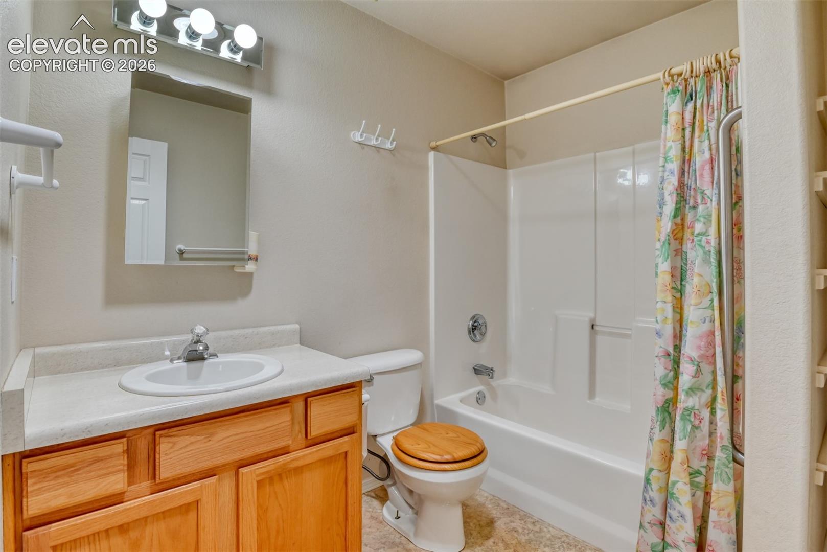 Full bathroom featuring a wood-finish vanity, integrated countertop with a recessed basin, white molded tub-shower surround, and wall-mounted vanity lighting