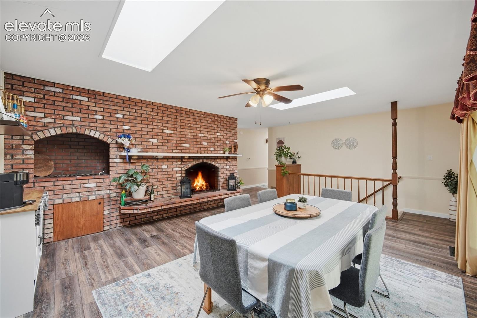 Brick hearth featuring an integrated masonry fireplace and alcove, wood-finish flooring, dual skylights, and a wooden baluster railing