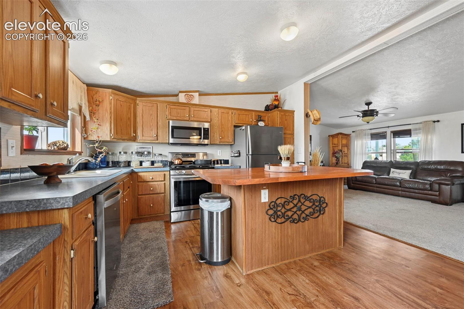 Kitchen featuring oak-finish cabinetry, central island with wood countertop, stainless steel appliances, and wood-finish flooring